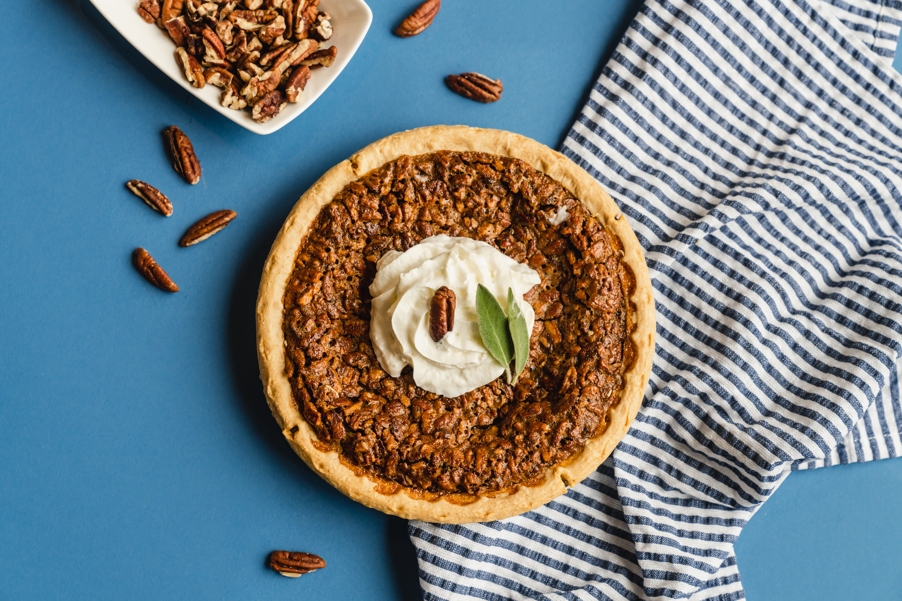 Full pecan pie with whipped cream seen from above on a blue table.