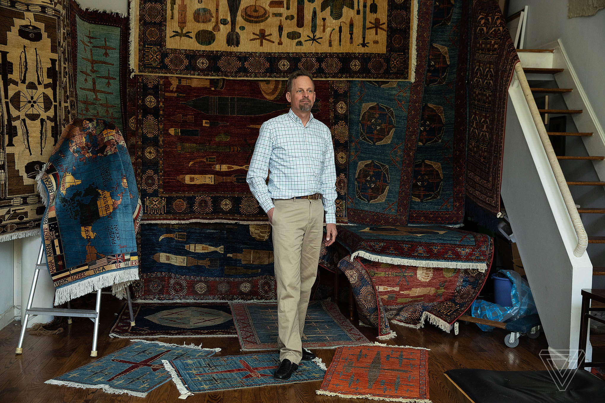 Kevin Sudeith surrounded by war rugs in vibrant red and blue patterns.