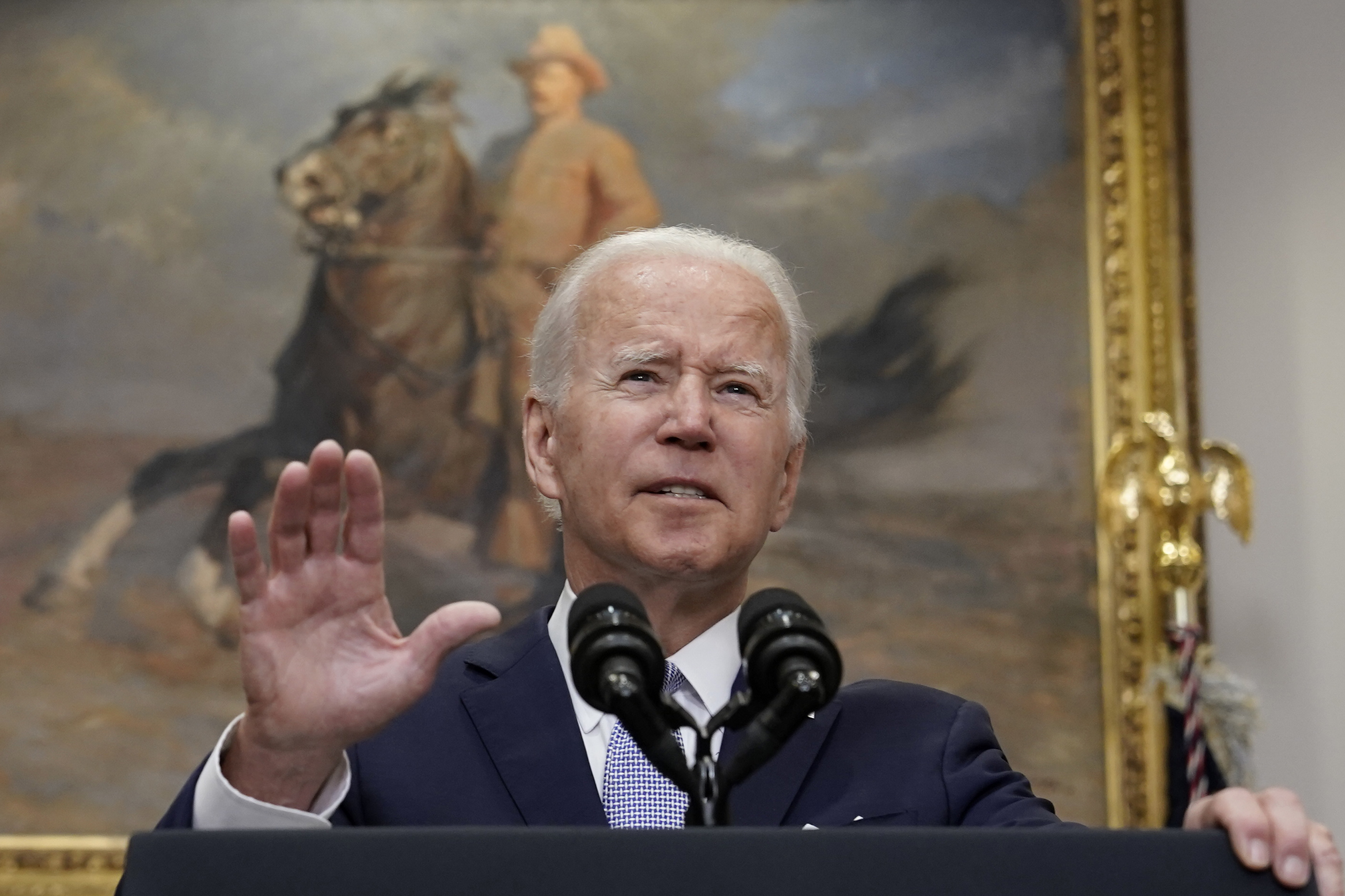 President Biden speaking into microphones in front of a picture of Teddy Roosevelt on a horse.