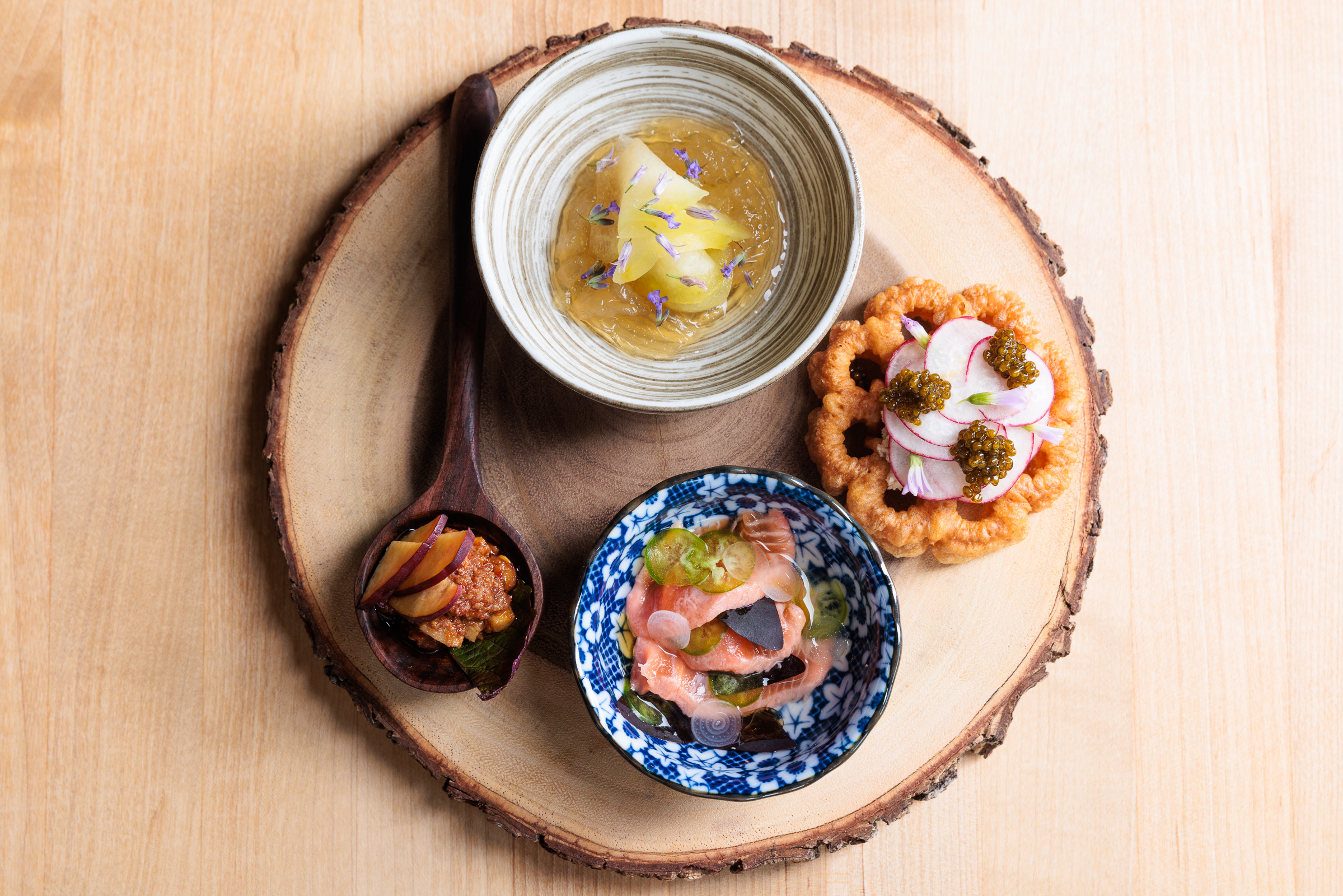 Pea gelee, rosettes with chickpea miso and butter, rainbow trout, and red fish ‘nduja all sit in separate ramekins on a round wooden platter