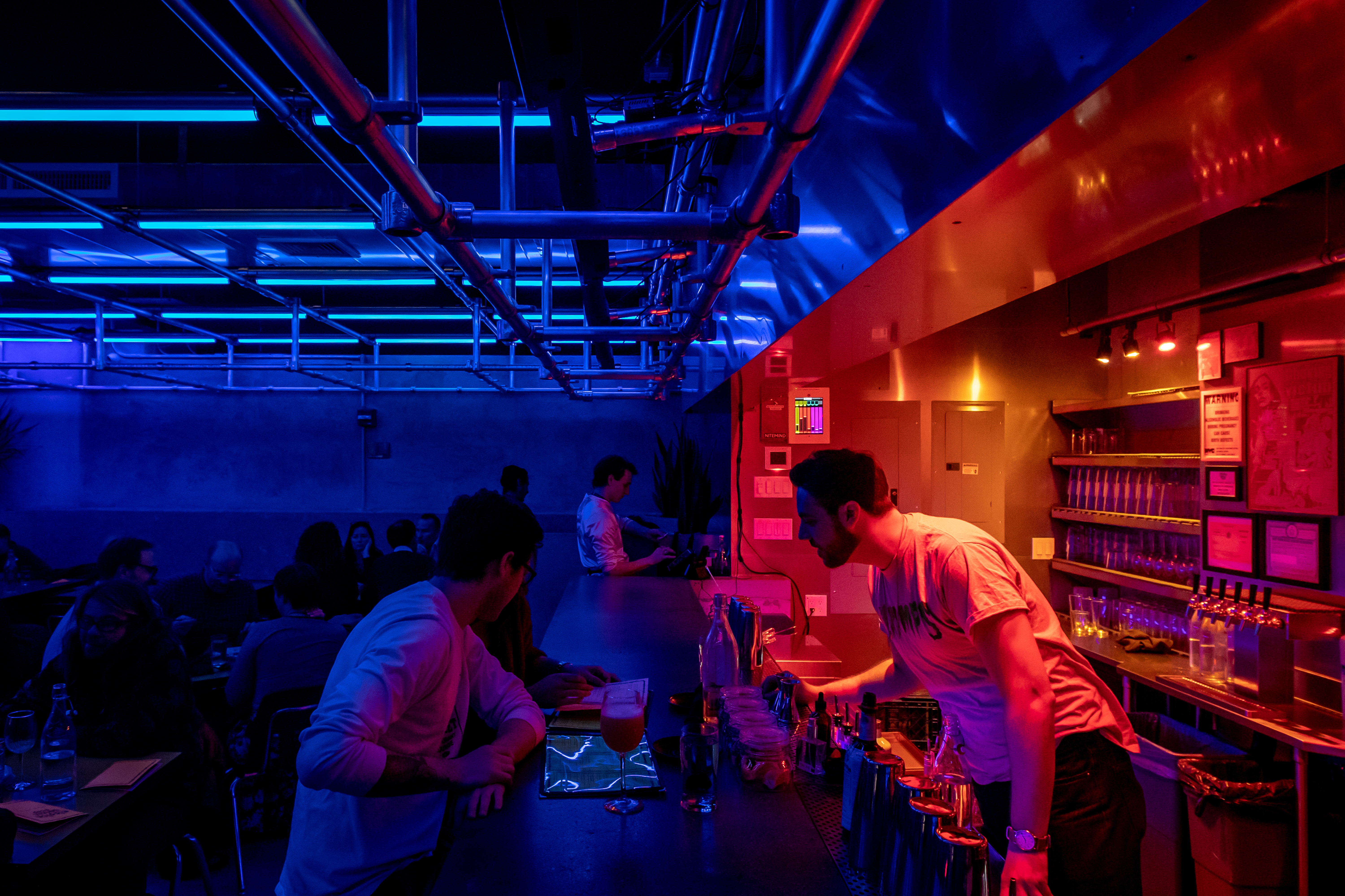 A dimly lit bar with red and blue neon lights in an industrial space.