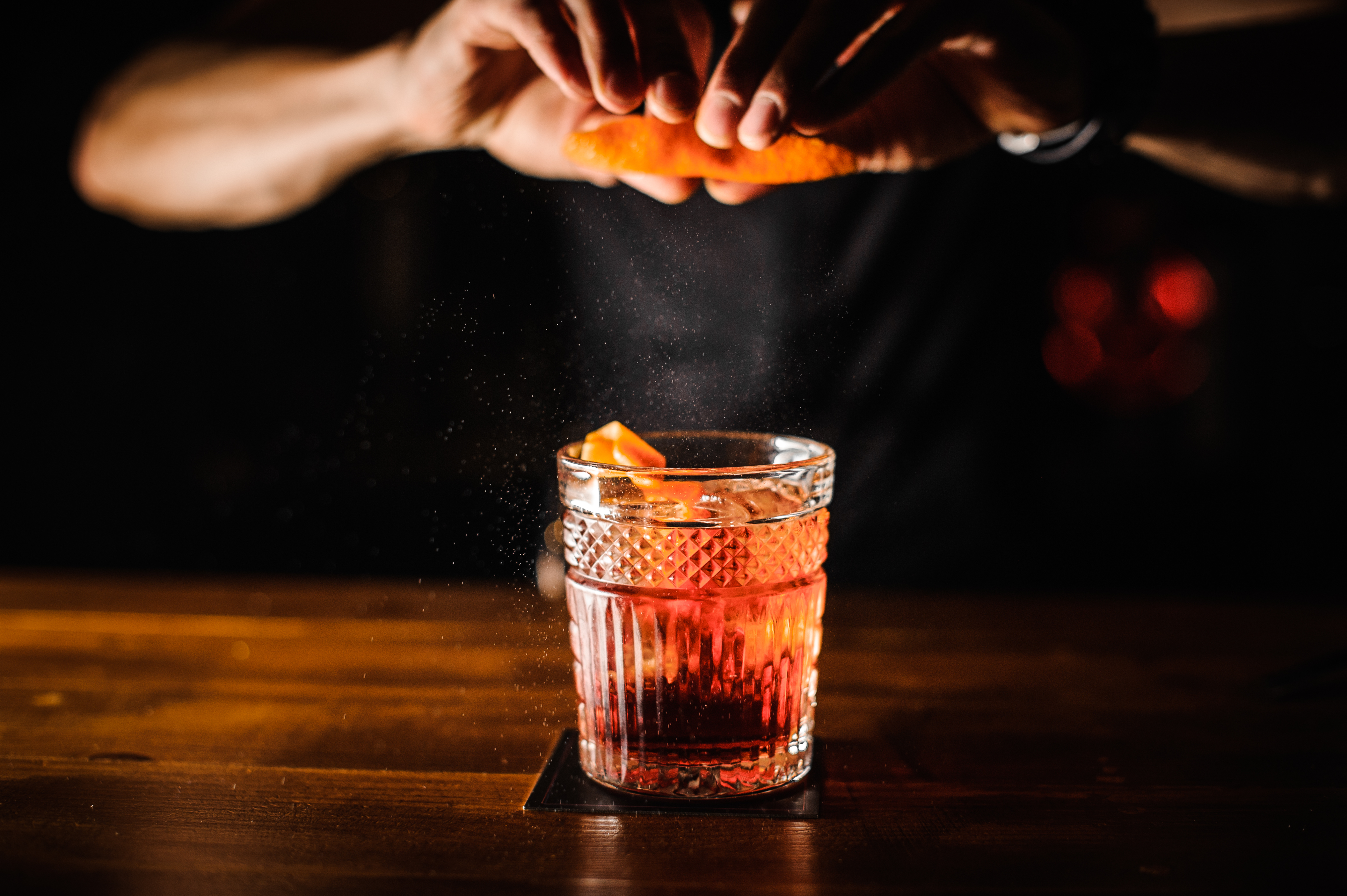 A cocktail gets spritzed with an orange peel.
