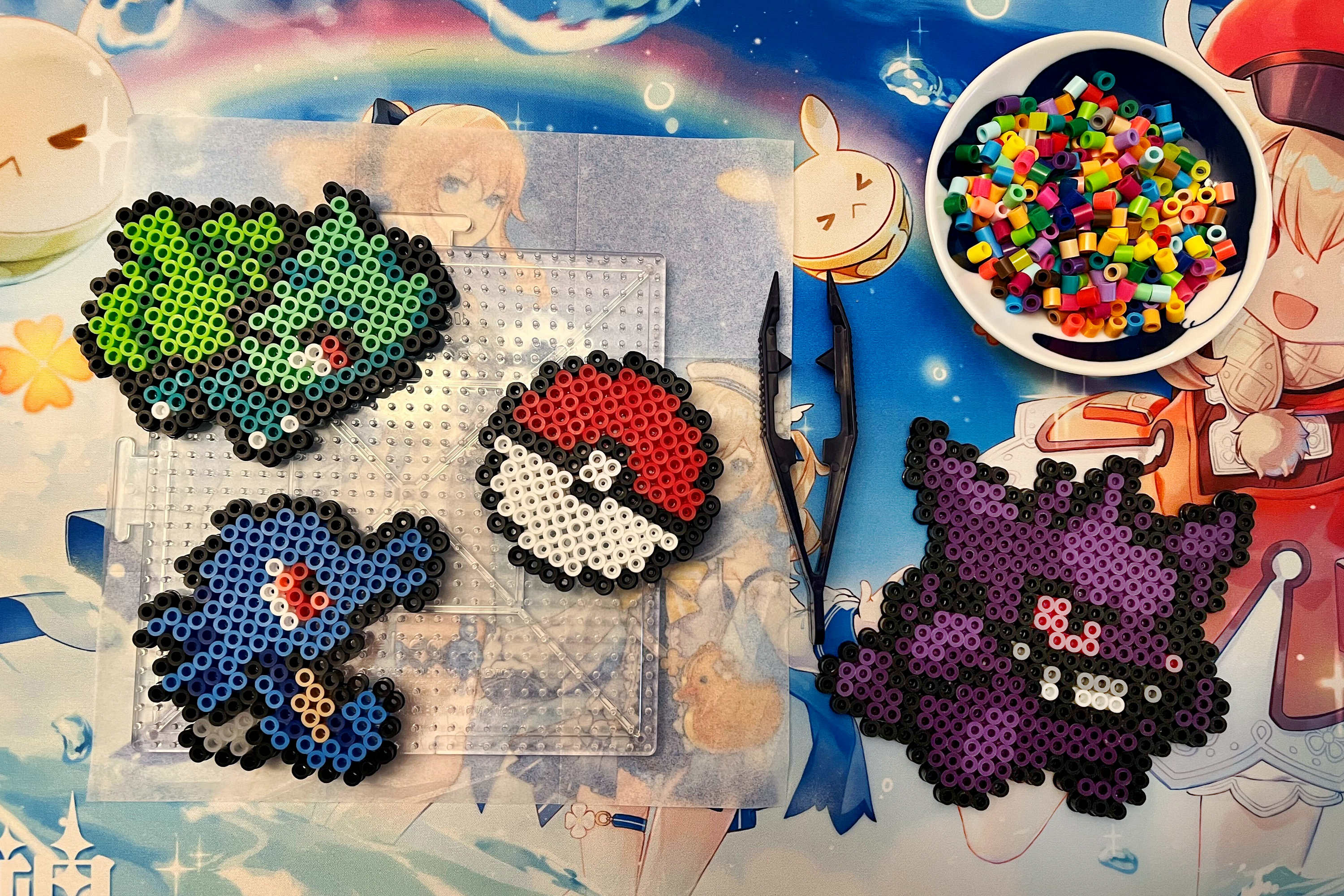 an image of perler bead pokemon on a desk mat. there’s a bulbasaur, gengar, horsea, and a poke ball.