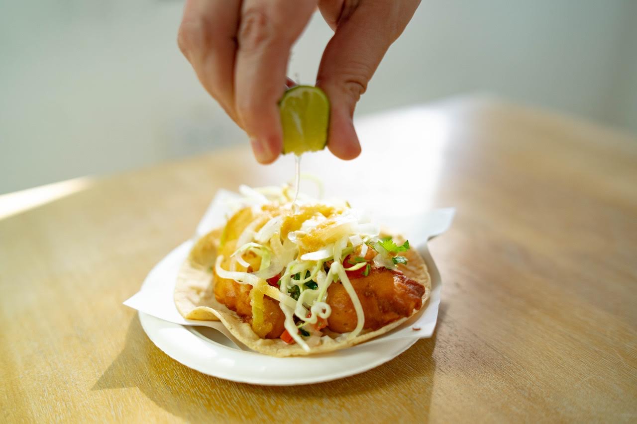 A hand squeezing a lime onto a fish taco.