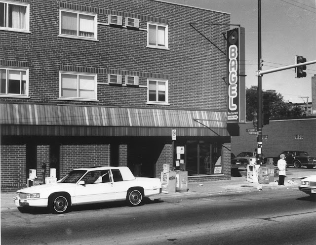 A black and white vintage photograph of a restaurant exterior with a sign that reads “The Bagel.”