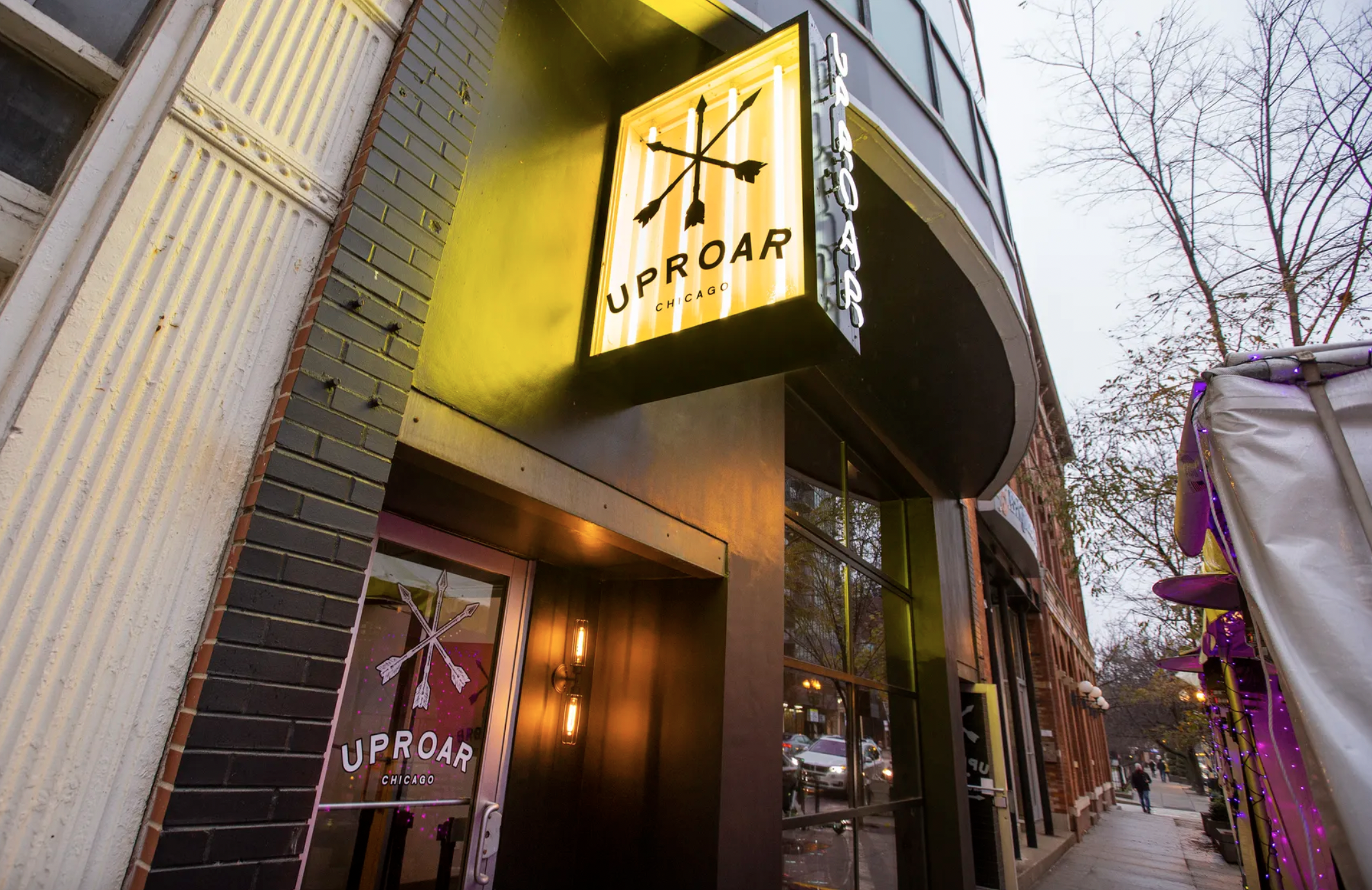 A black-painted brick restaurant exterior with a yellow sign that reads “Uproar.”