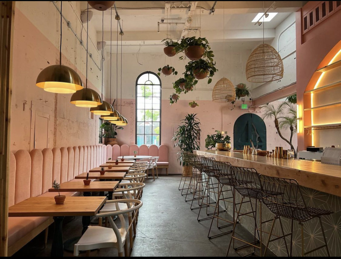 Pink walls and velveteen banquettes line the wall of Bar Cala in Portland, with a back-lit bar and hanging plants.
