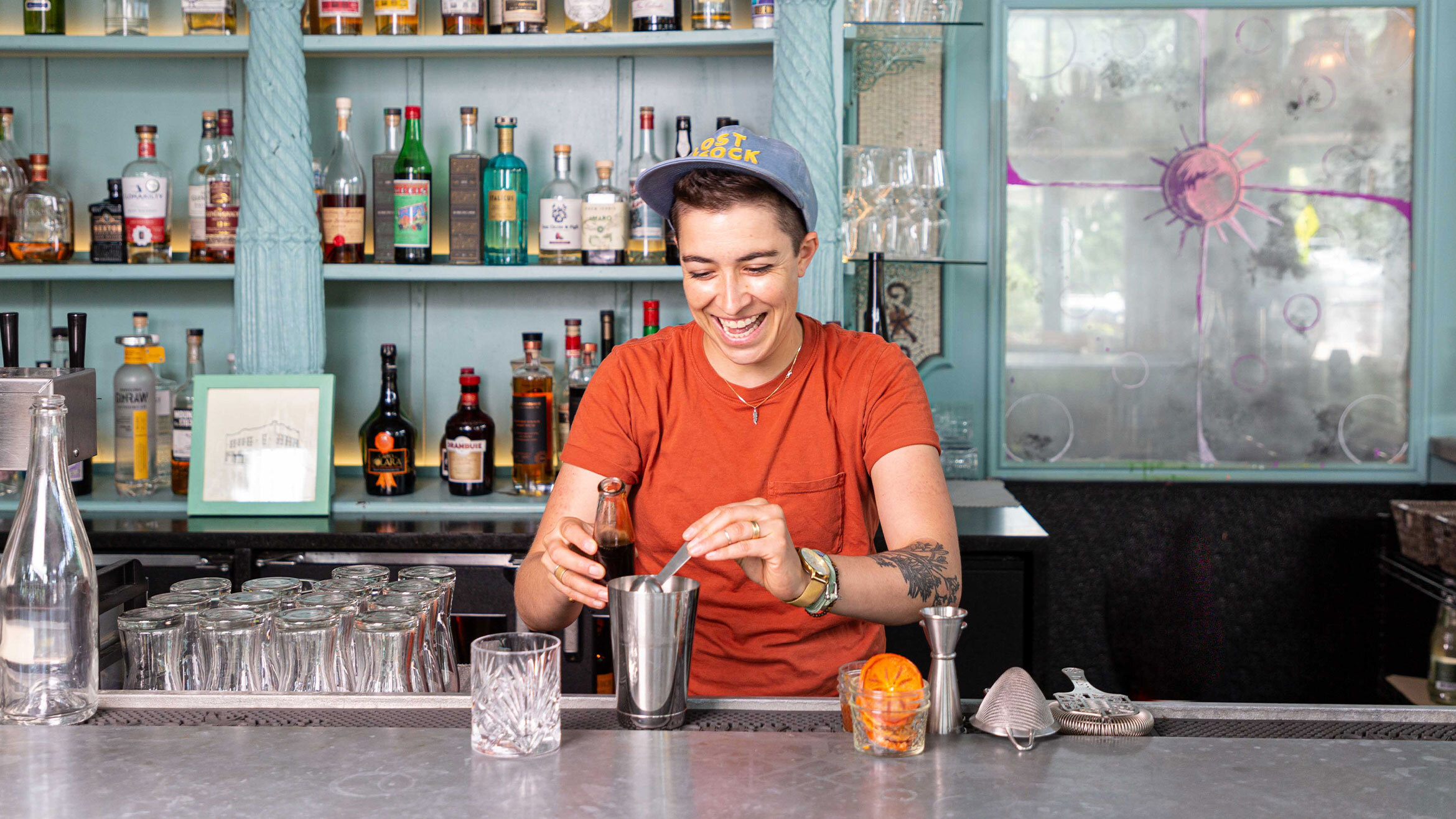 A bartender creating a cocktail behind a bright bar.