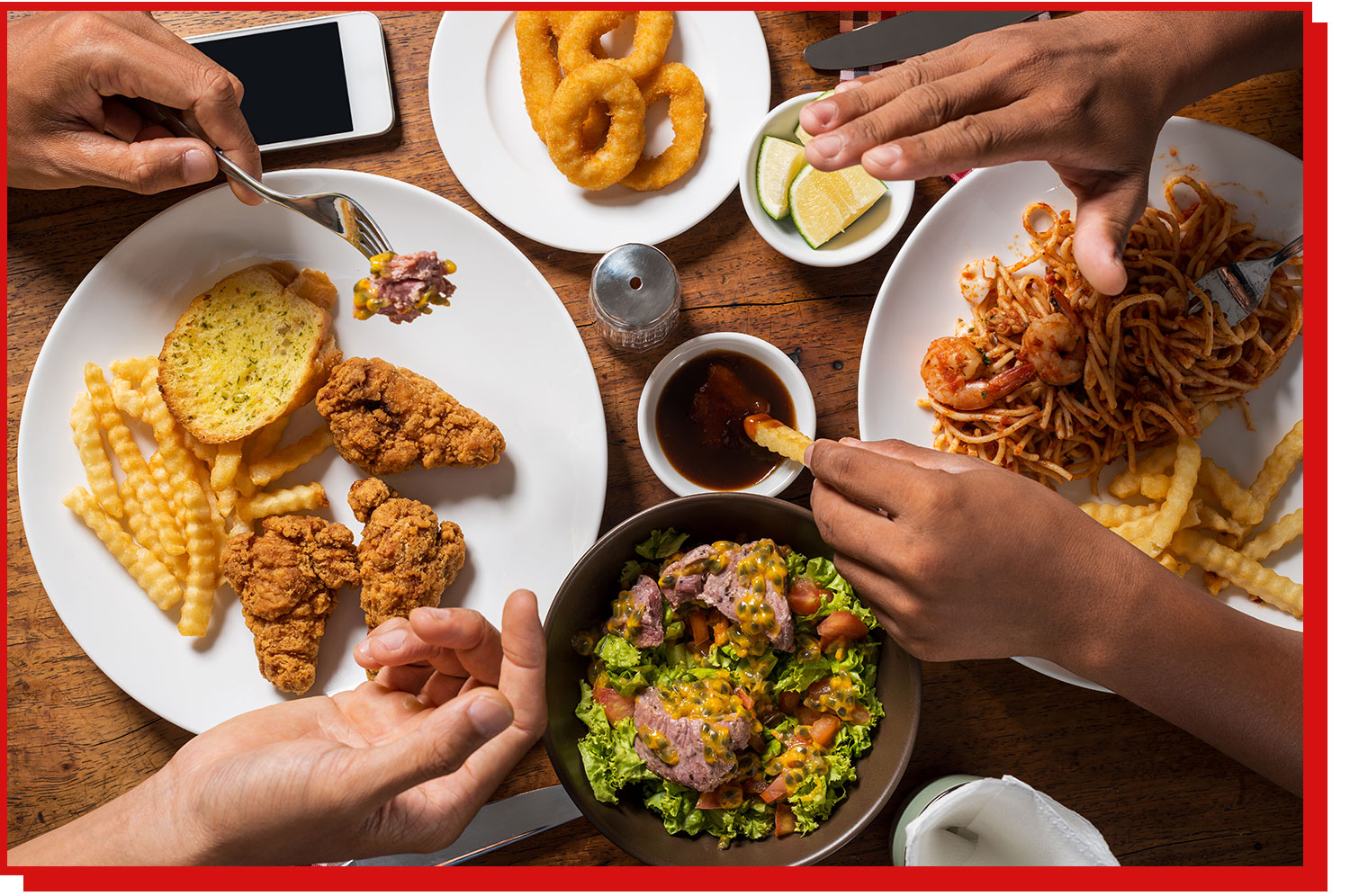A table laden with food and one person eating it with their hands while the other holds a fork 