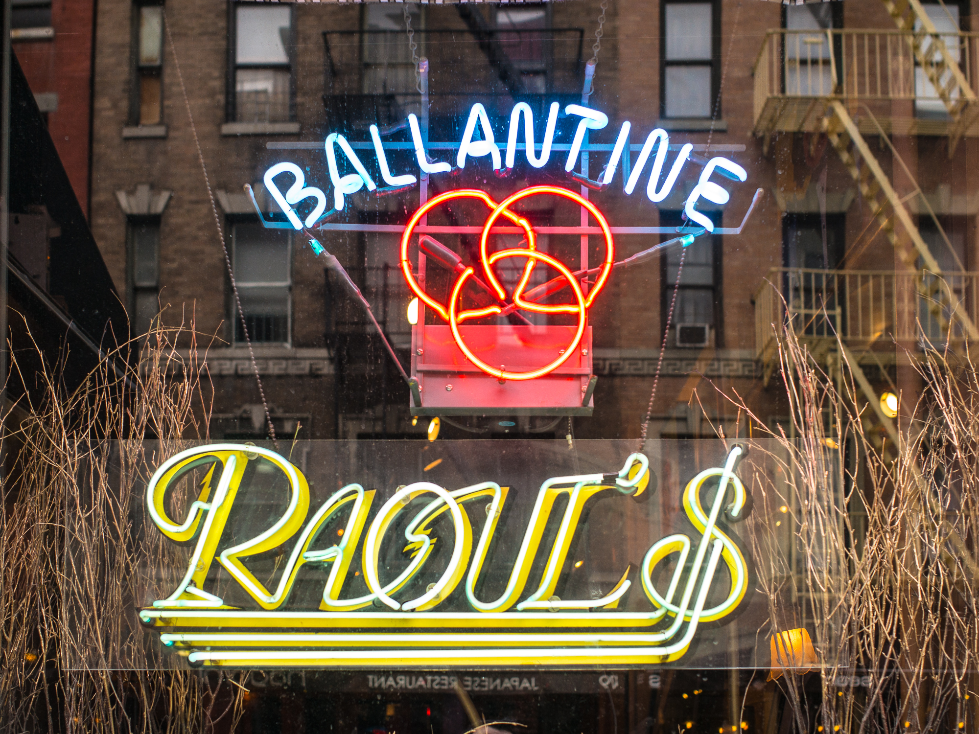 A neon sign with the words “Ballantine Raoul’s” gleams on a glass window.