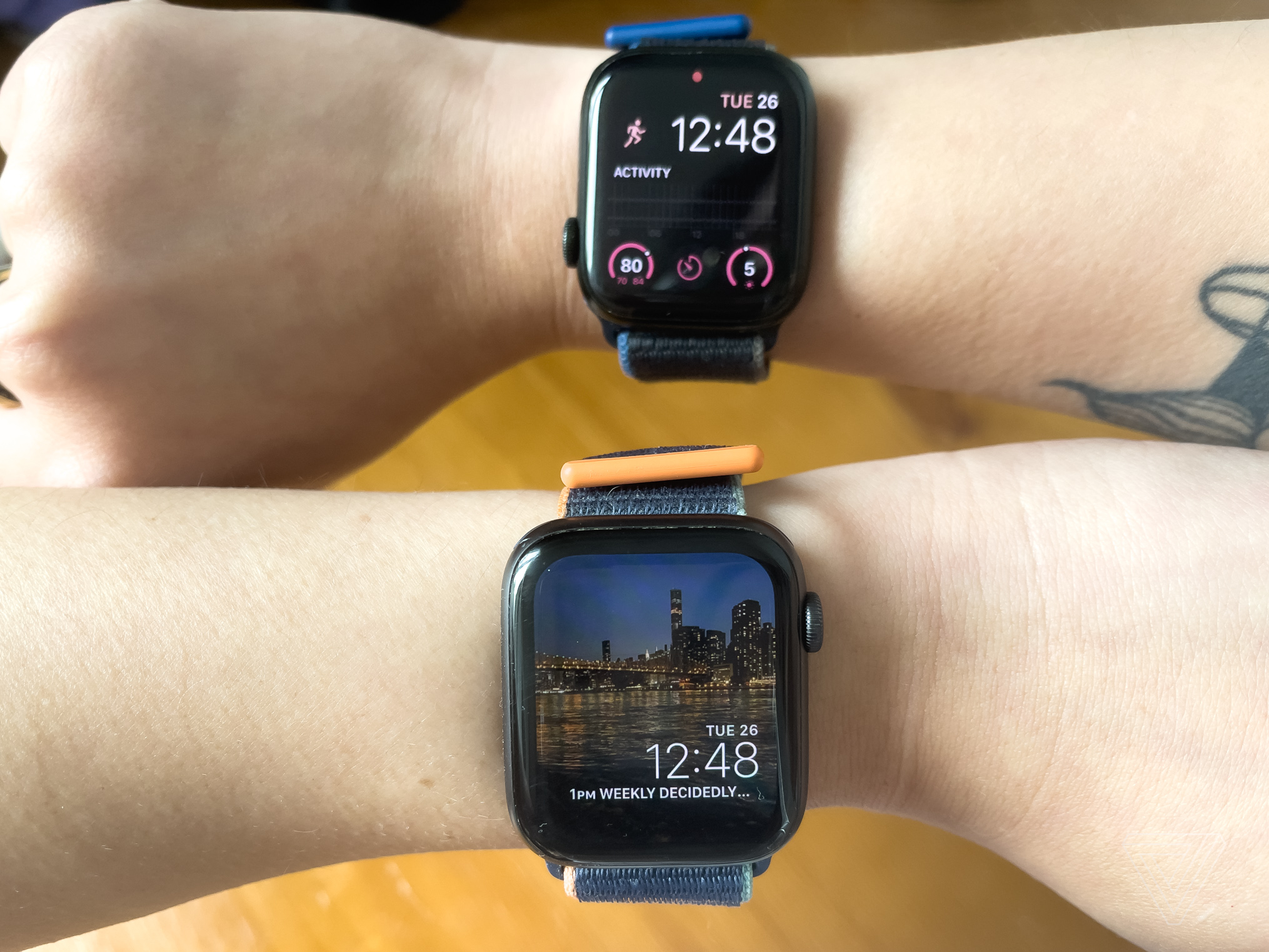 Two Apple Watches, one worn on the left wrist with the digital crown on the right, and the other on the right wrist with the crown on the left. 