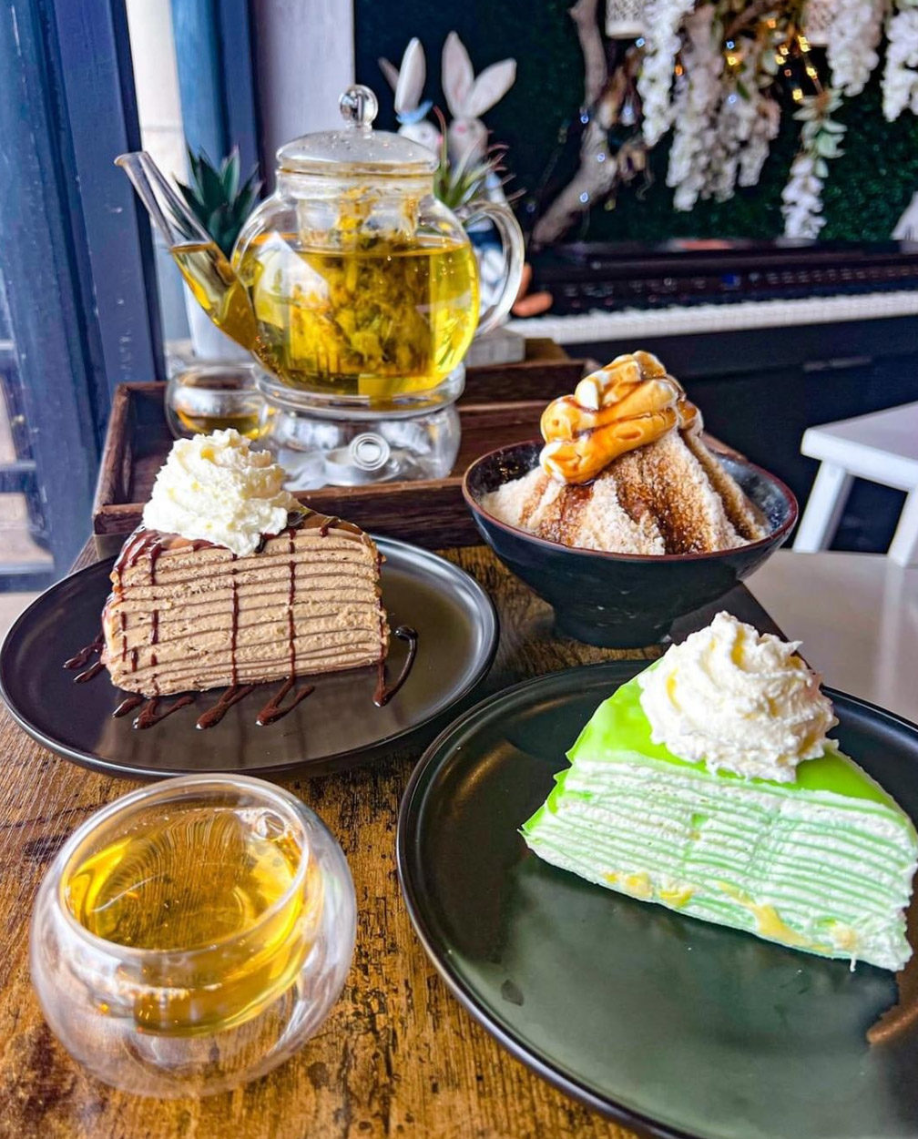 Two crepe layer cake slices on two plates with a pot of yellow tea and a glass of yellow tea. 