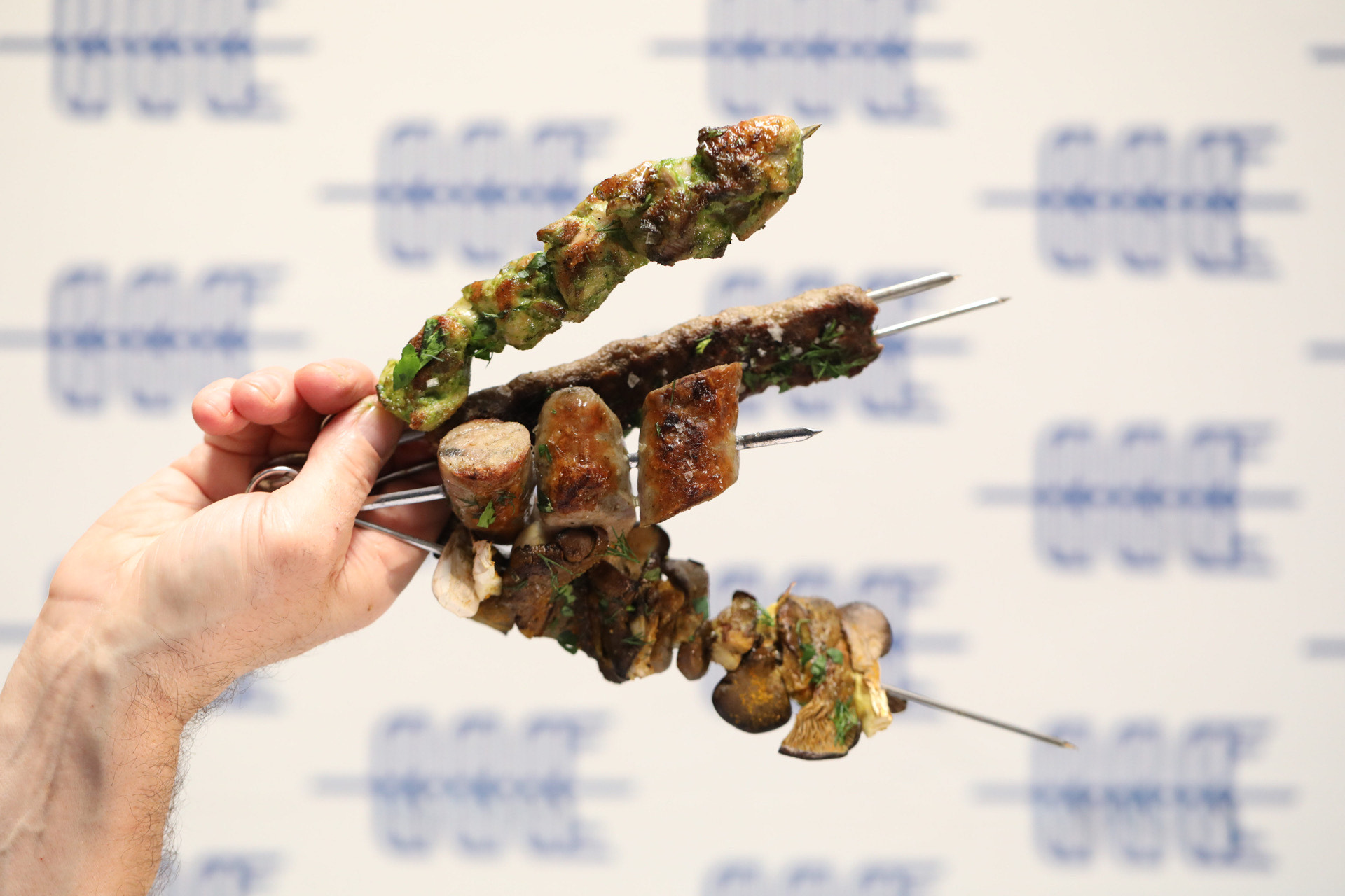 A hand holds a variety of meat skewers.