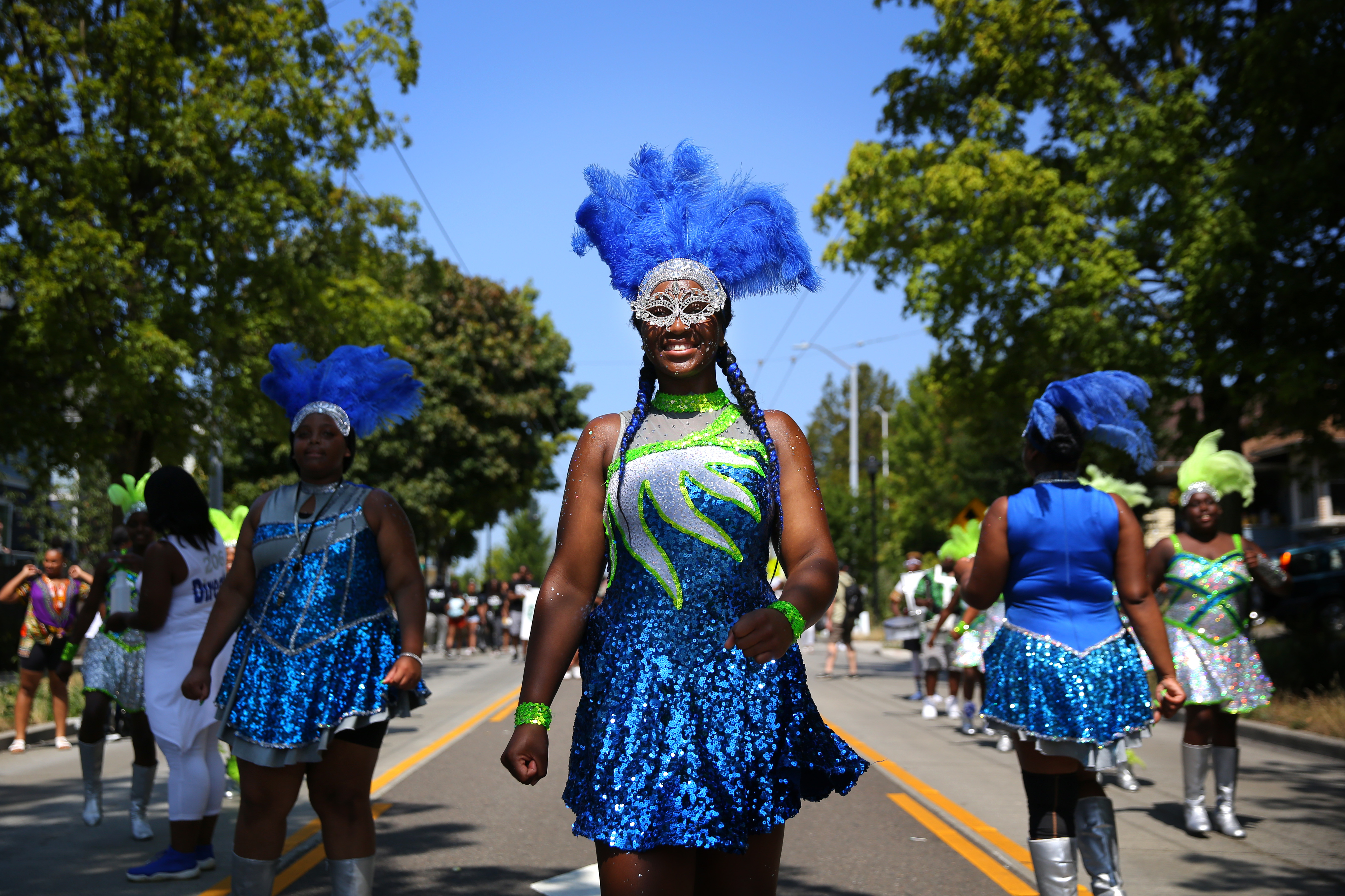 Three African American women in royal blue and green glittering costumes march down the main thoroughfare during a heritage parade in Seattle.