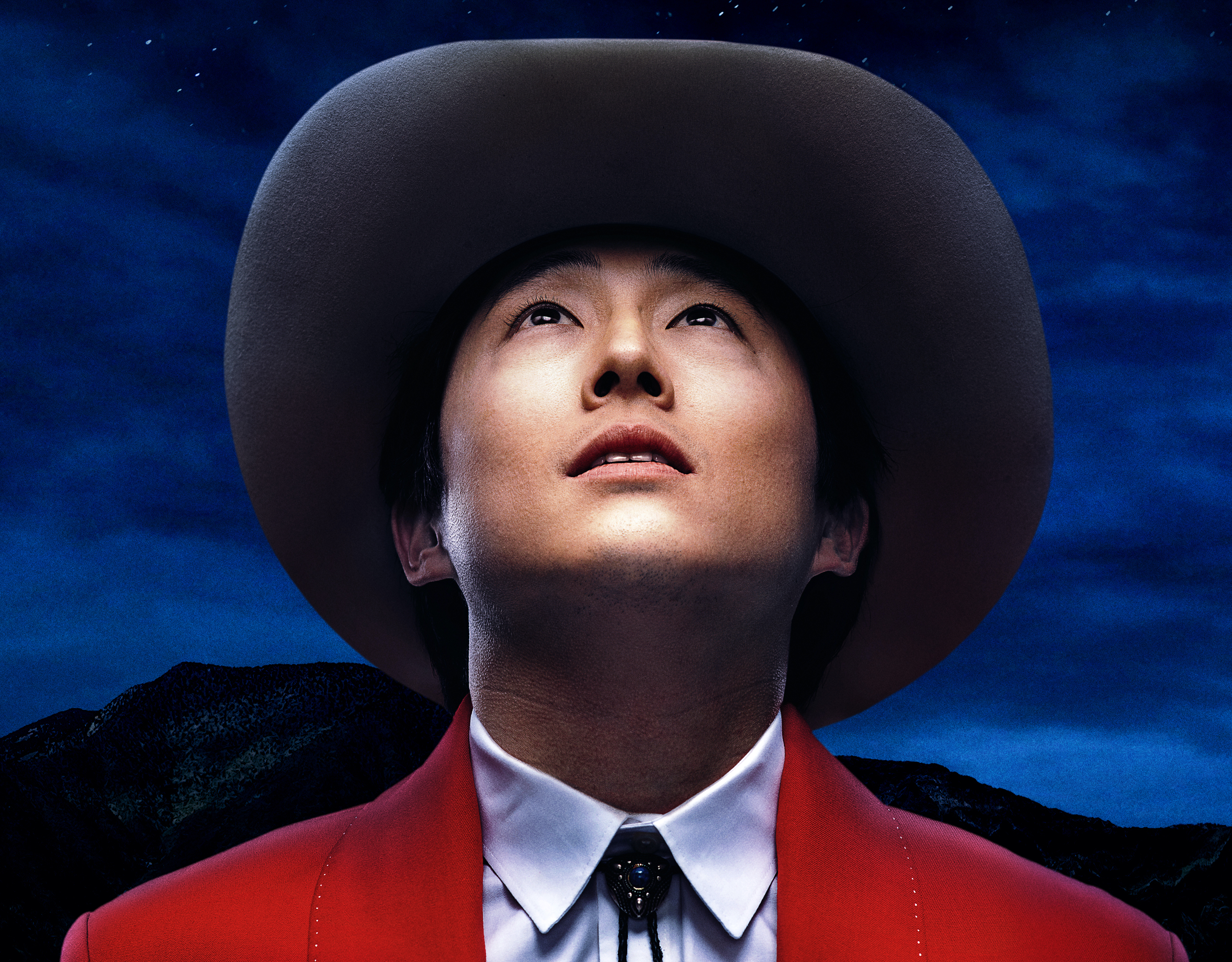 A poster image for Nope, with Steven Yuen as Ricky "Jupe" Park looking up at the sky in wonder