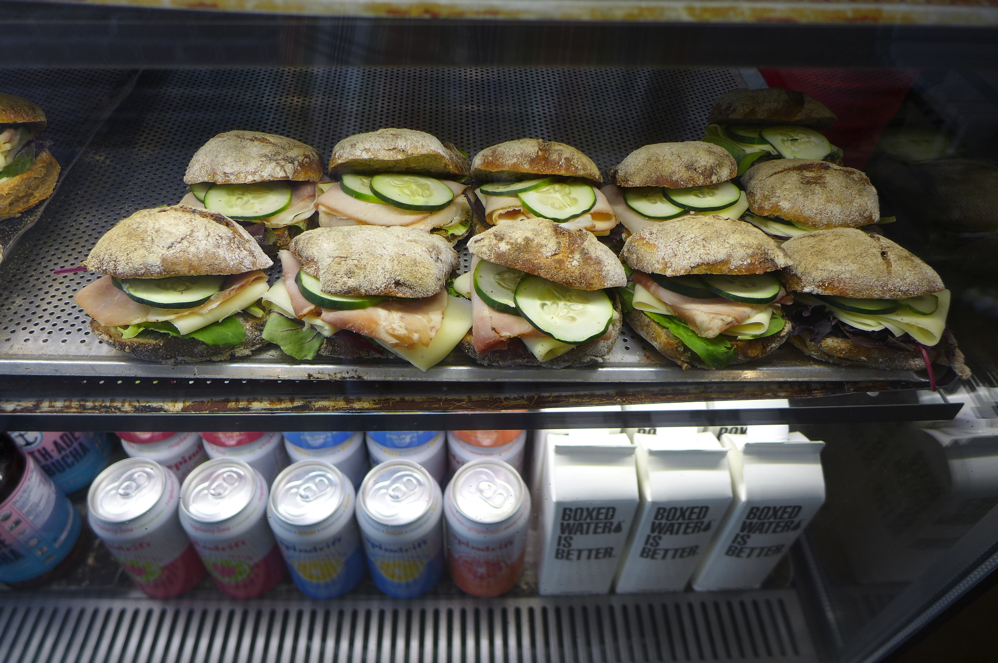 A glass case with sandwiches lines up.