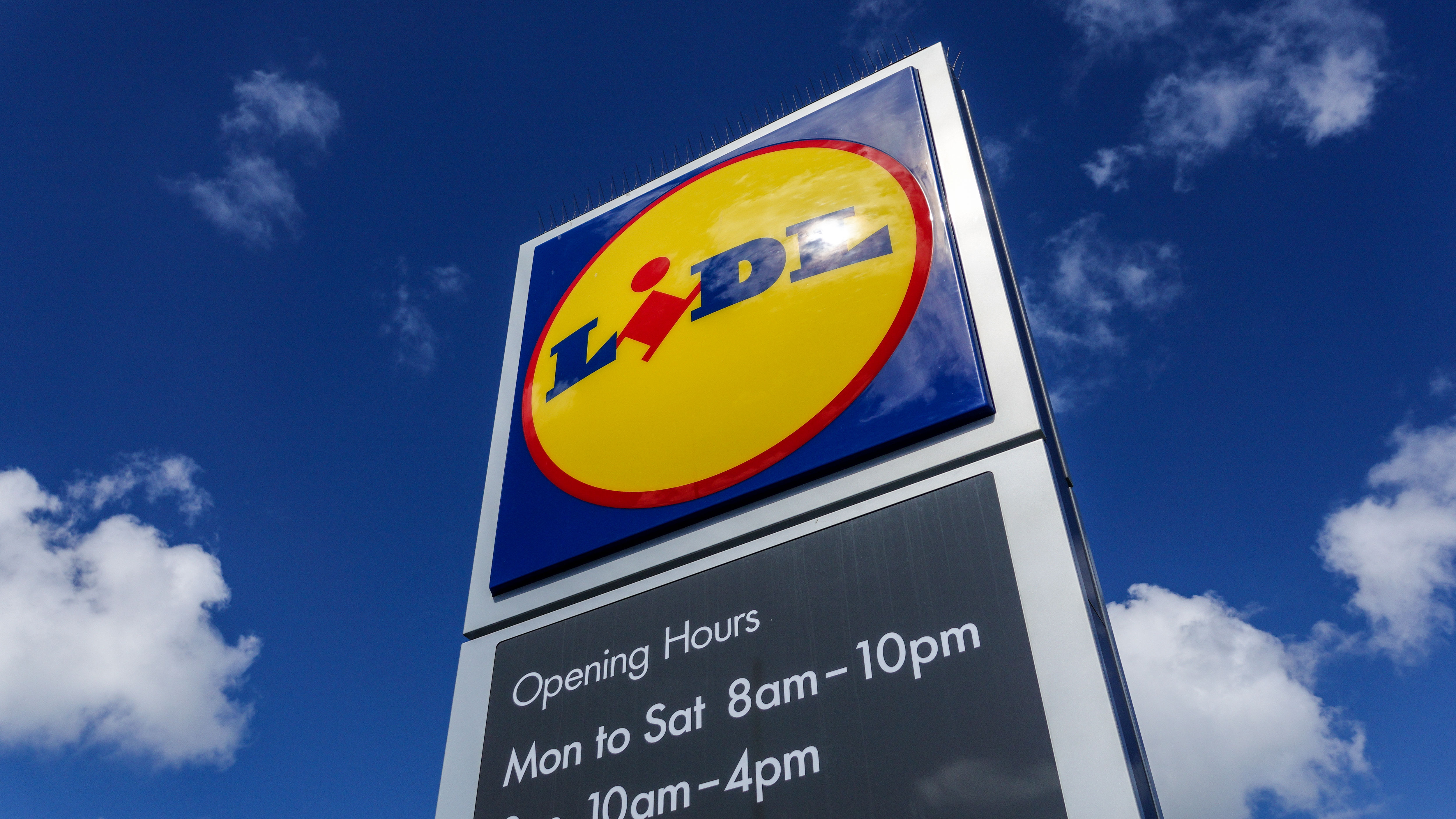 A sign with the logo of Lidl, a German discount grocery chain, gleams in the sun against a blue sky.