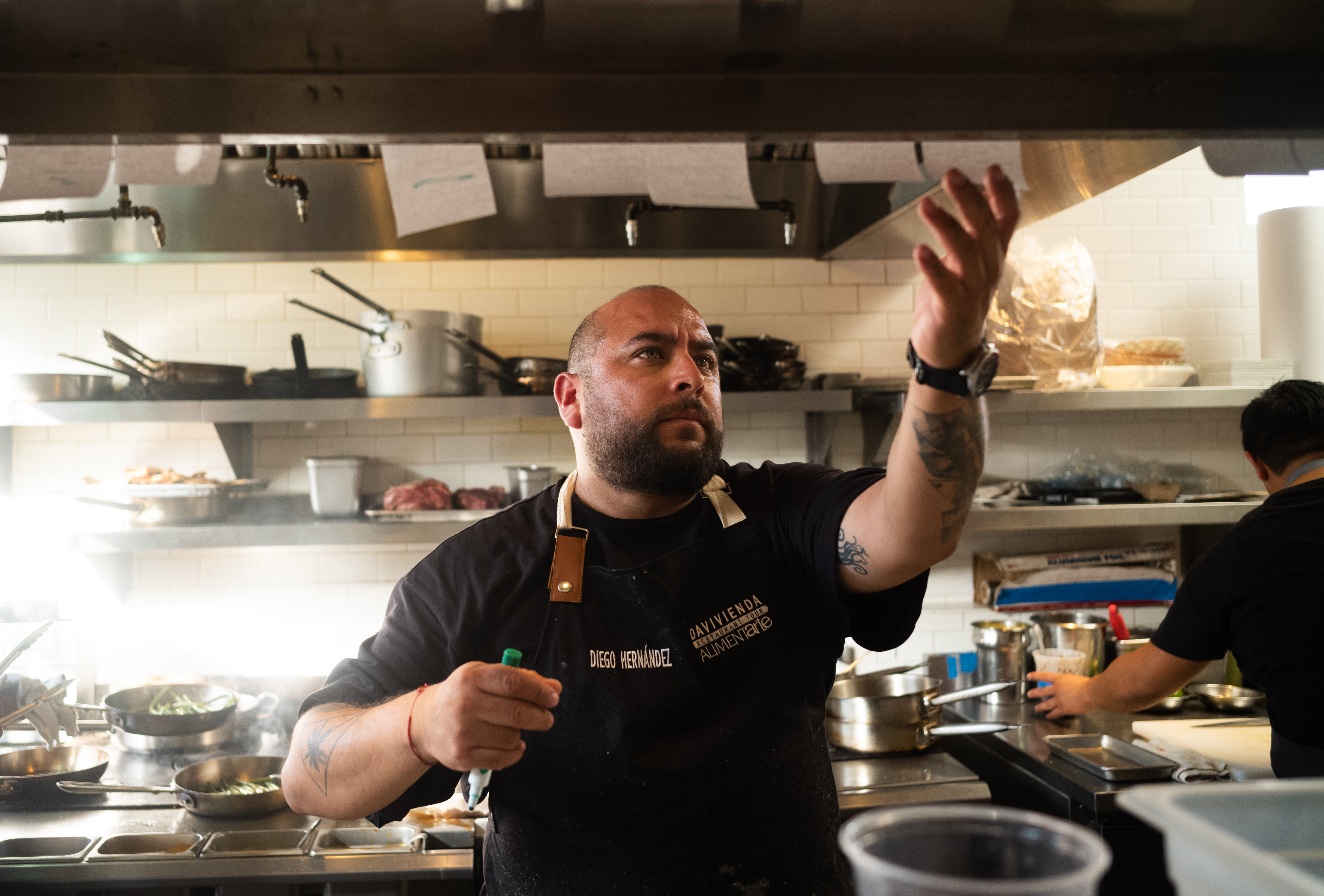 Chef wearing dark apron checks orders inside a restaurant kitchen.