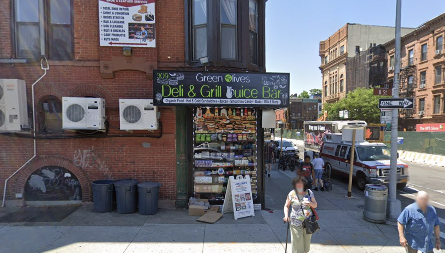 A red brick building with a corner bodega with a sign that reads Green Olives Deli &amp; Grocery.