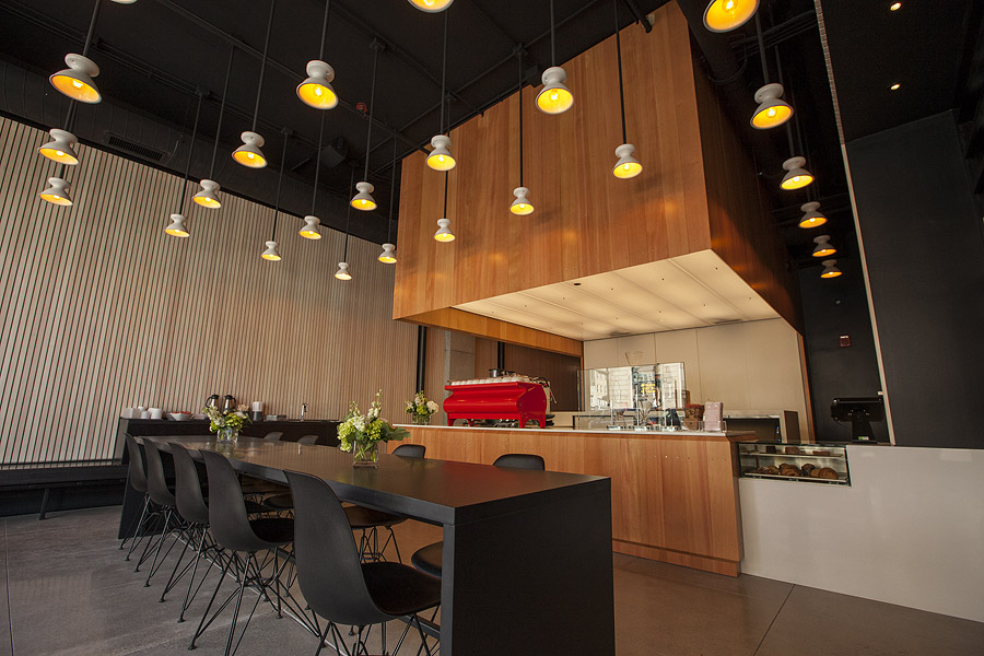A coffee bar and shop with a modern, geometric design, many hanging lamps, and a bright red espresso machine.