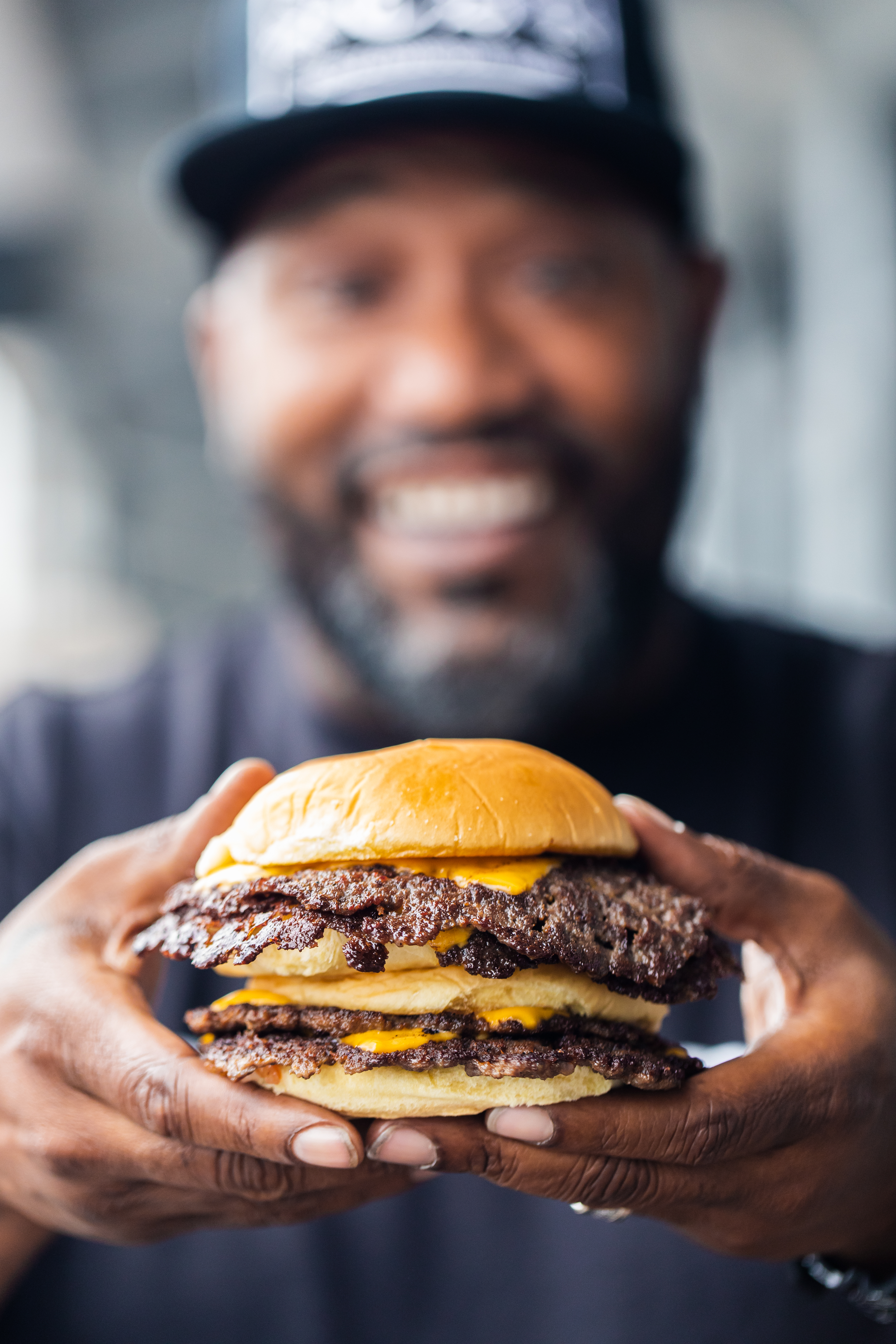 Bun B holding two double-patty Trill Burger smash burgers loaded with cheese.