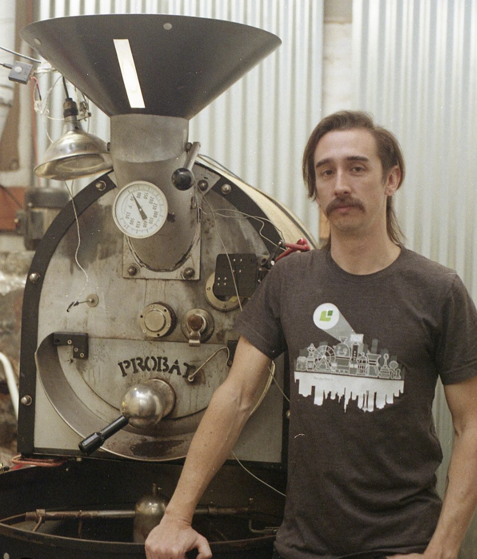 A man next to a coffee roaster.