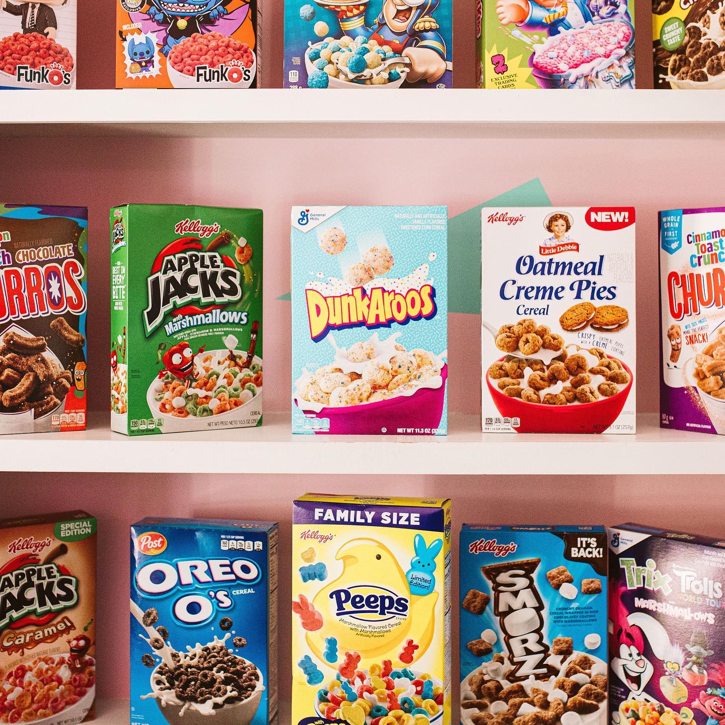 Powder pink shelves lined with name brand cereals like Apple Jacks, Dunkaroos, and Oatmeal Cream Pies from Day and Night Cereal Bar. 