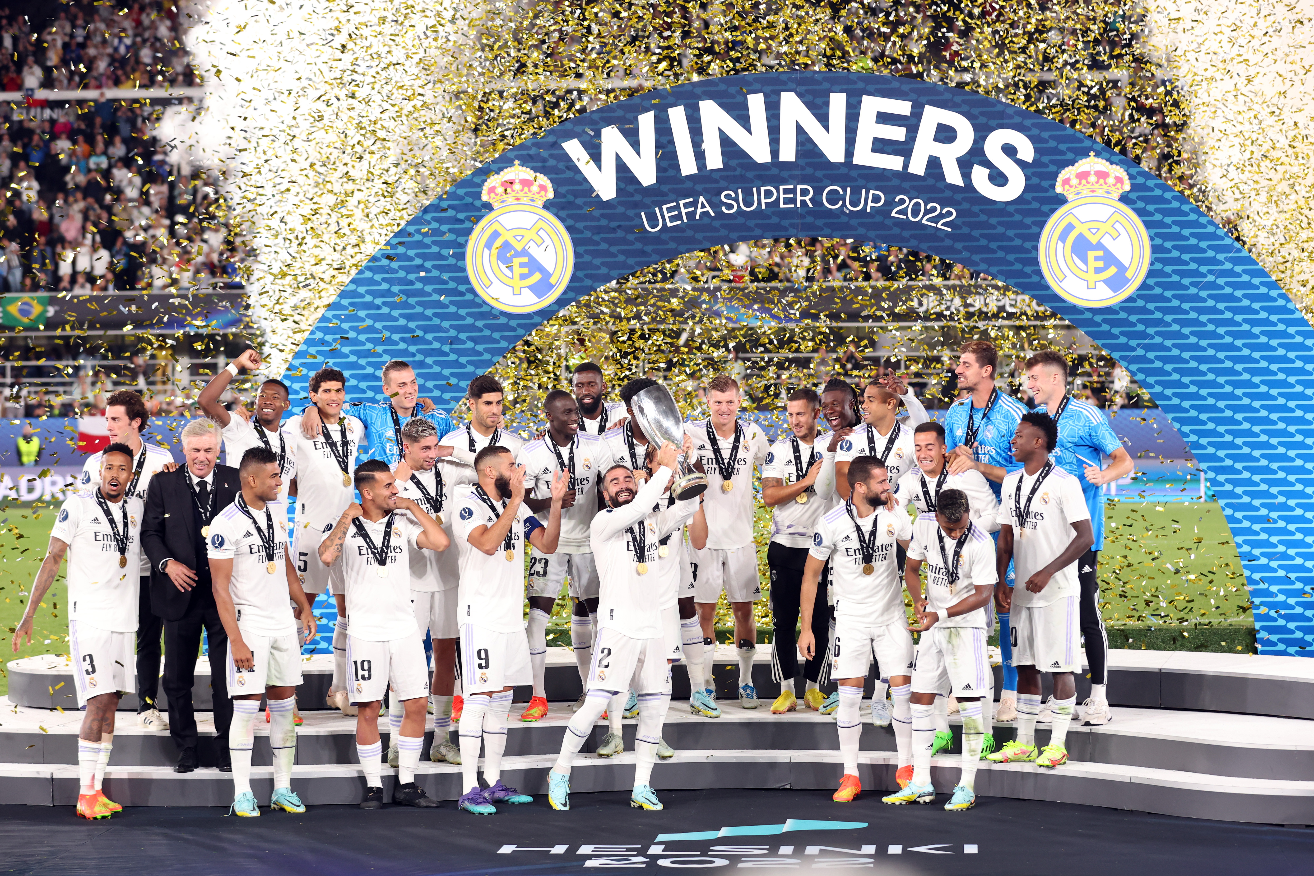 The players of Real Madrid celebrate with a trophy in front of a giant white and blue banner that says WINNERS