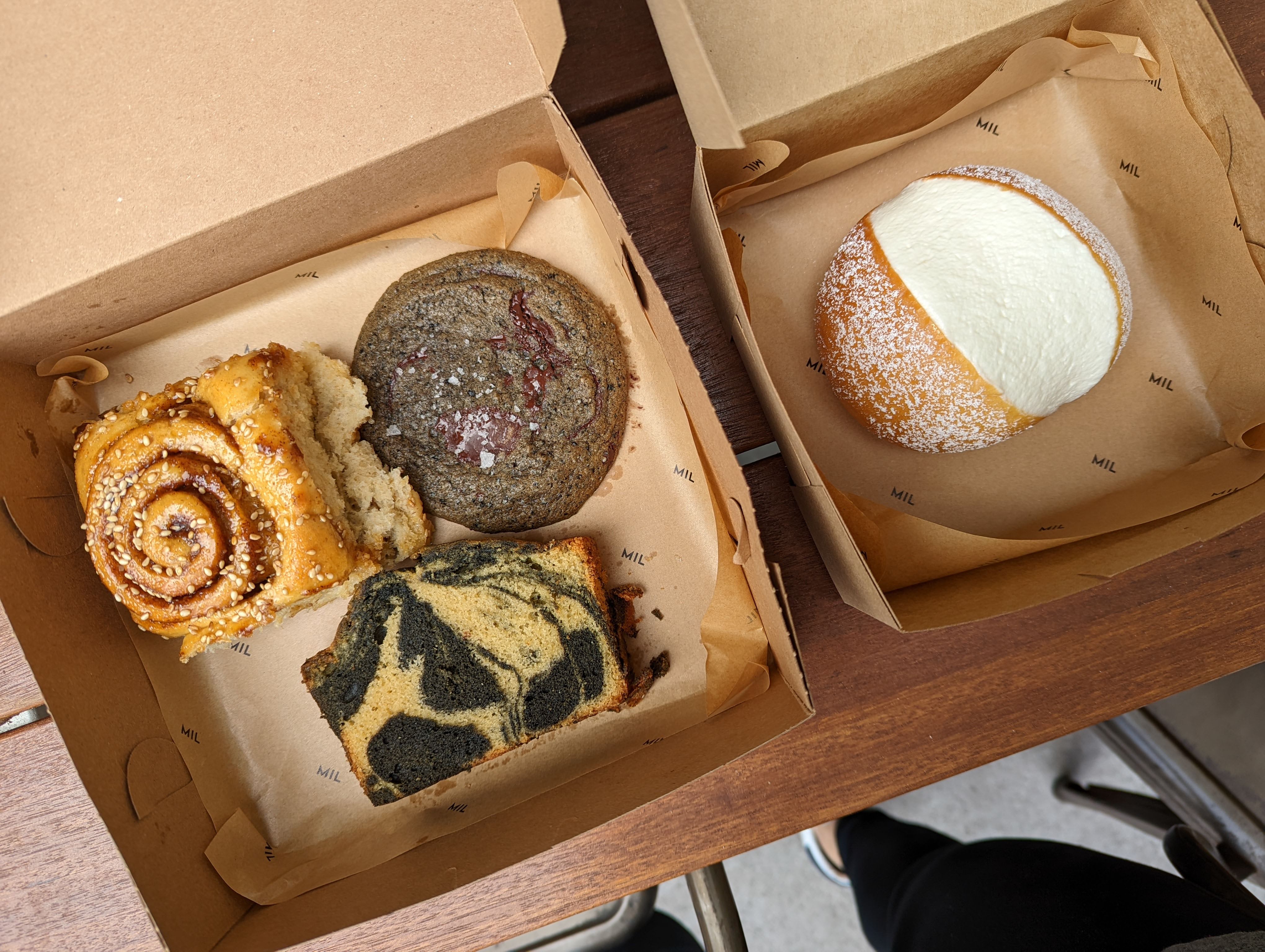 Two cardboard boxes filled with a cinnamon bun, pound cake, cookie, and milk cream bun.