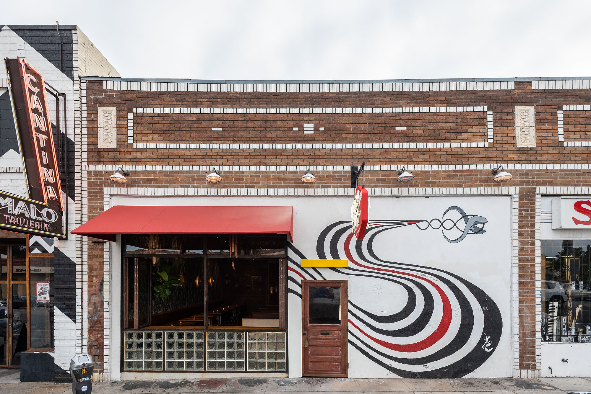 A red awning and white mural on a brick building during a cloudy day.