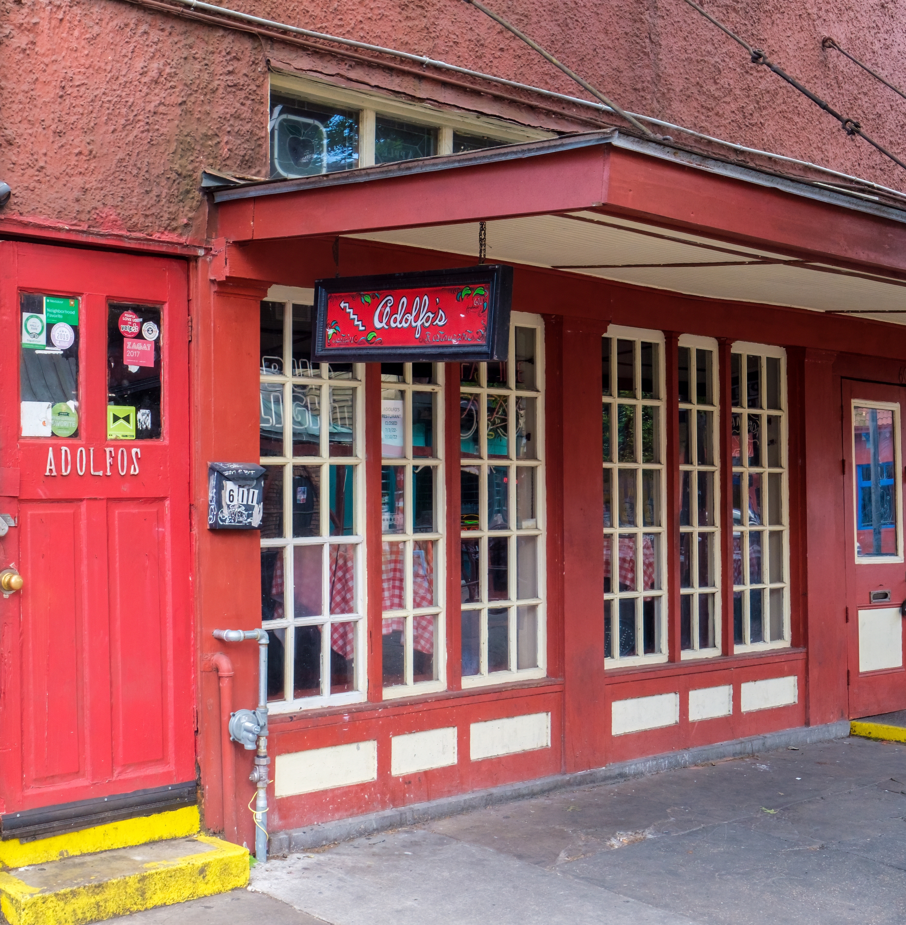 The outside facade of Adolfo’s Restaurant on Frenchmen Street in New Orleans’s Marigny neighborhood including a red door and awning.