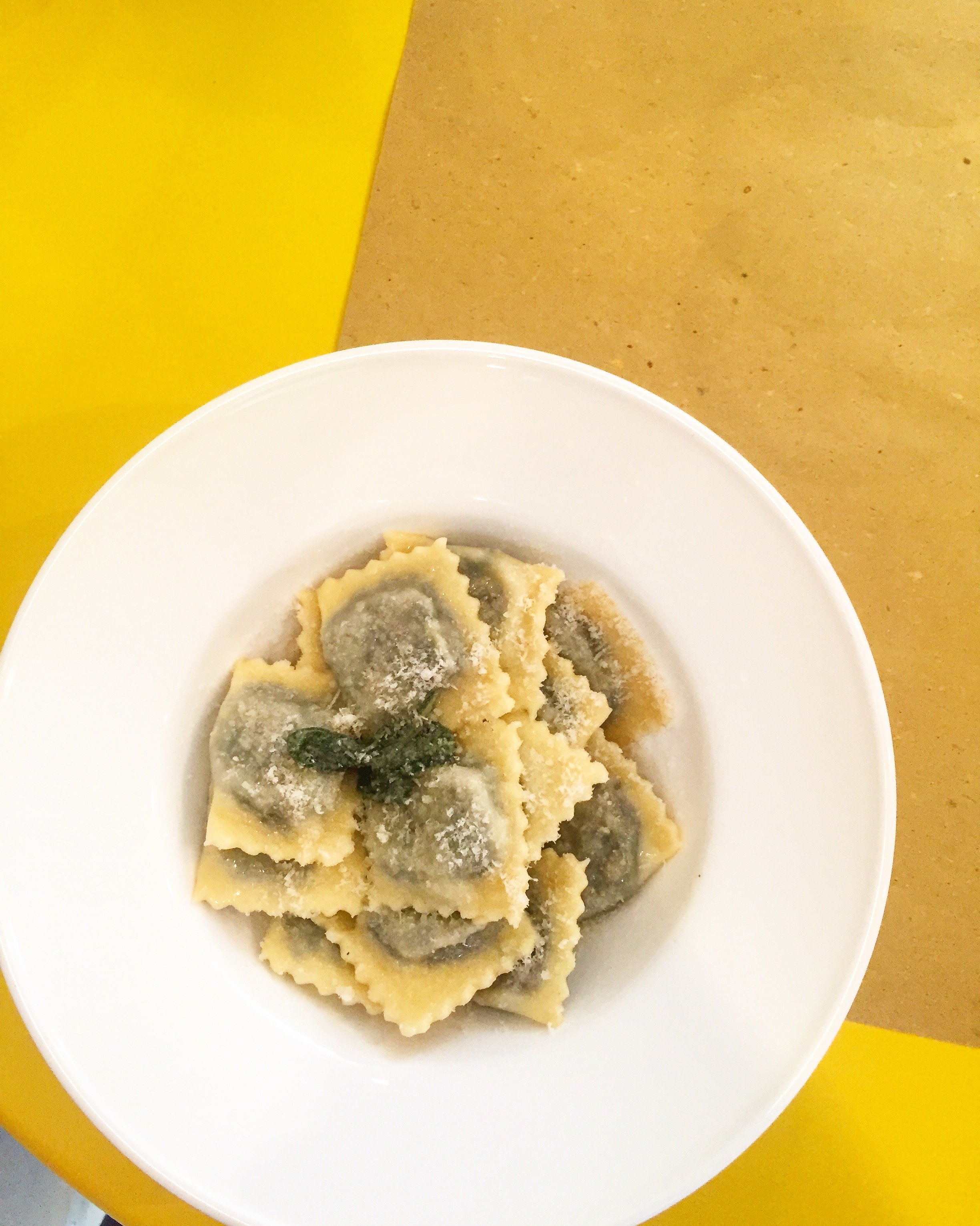 A white plate of ravioli on a yellow table