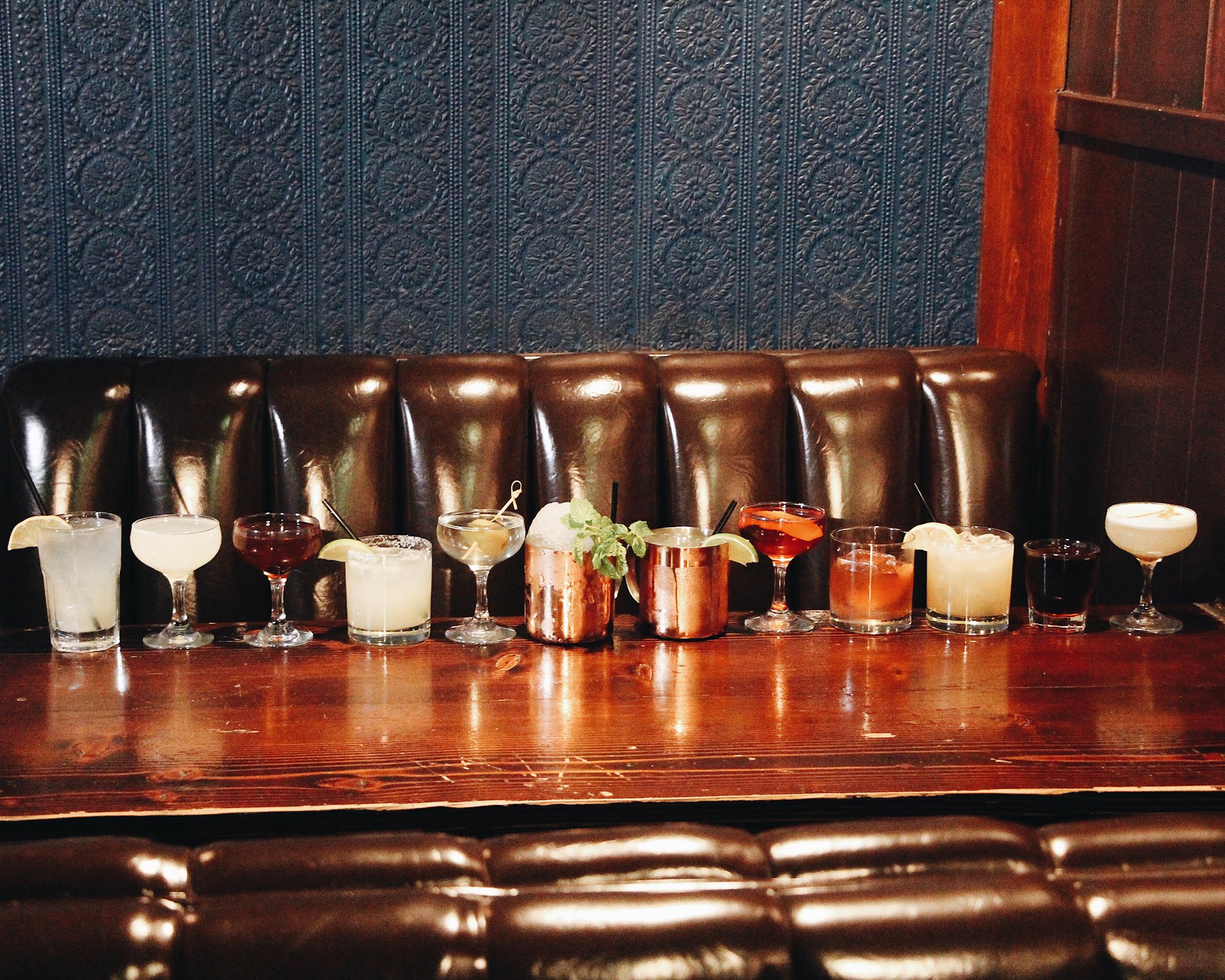 A run of a dozen drinks in various glasses along a wooden bar.