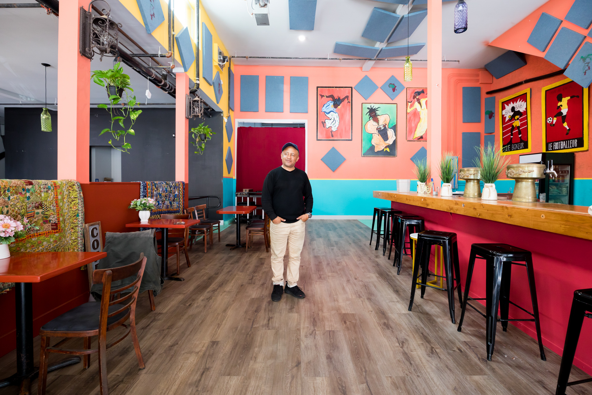 Owner Marco Senghor wears a black long sleeve shirt and stands inside the colorful new Big Baobab in the Mission.