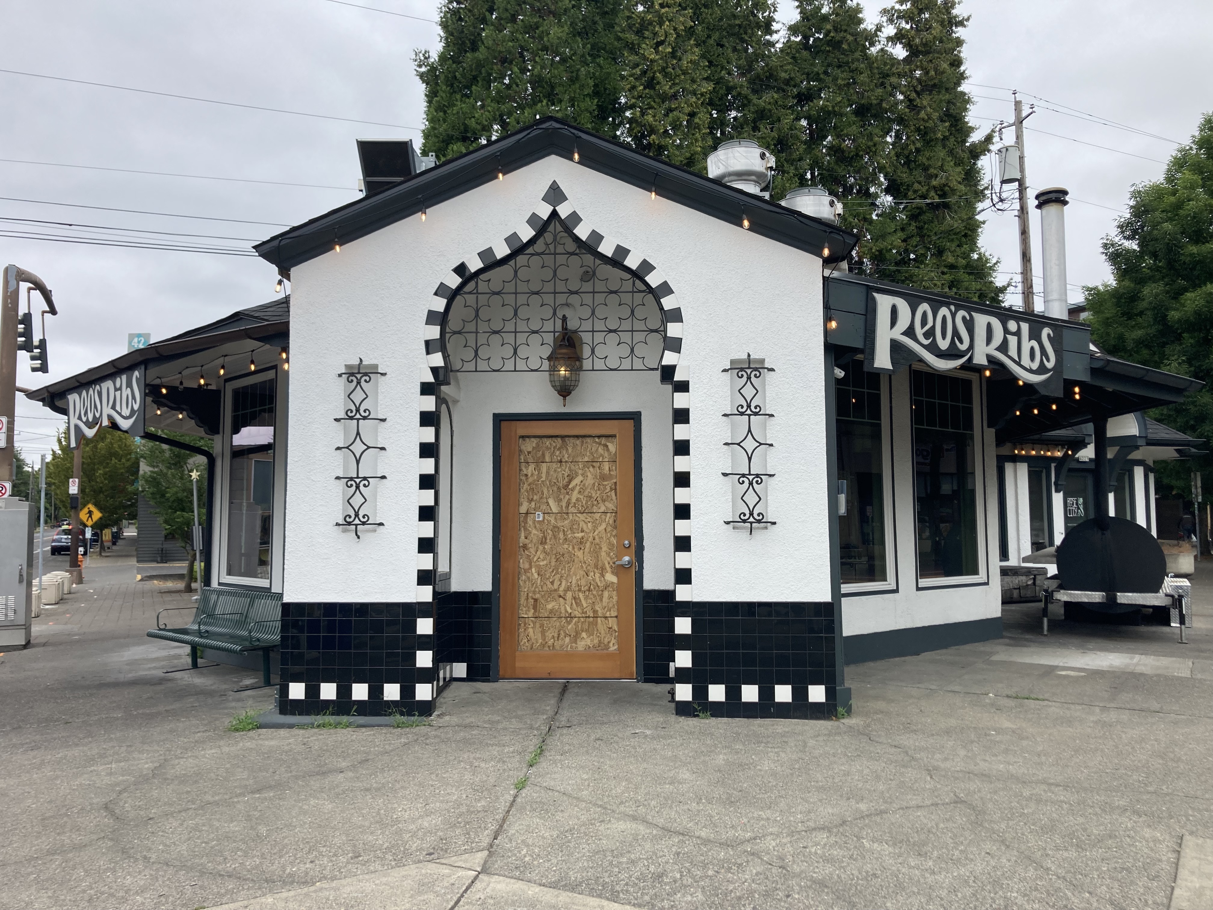 The exterior of Reo’s Ribs’ black-and-white building with a boarded up door.