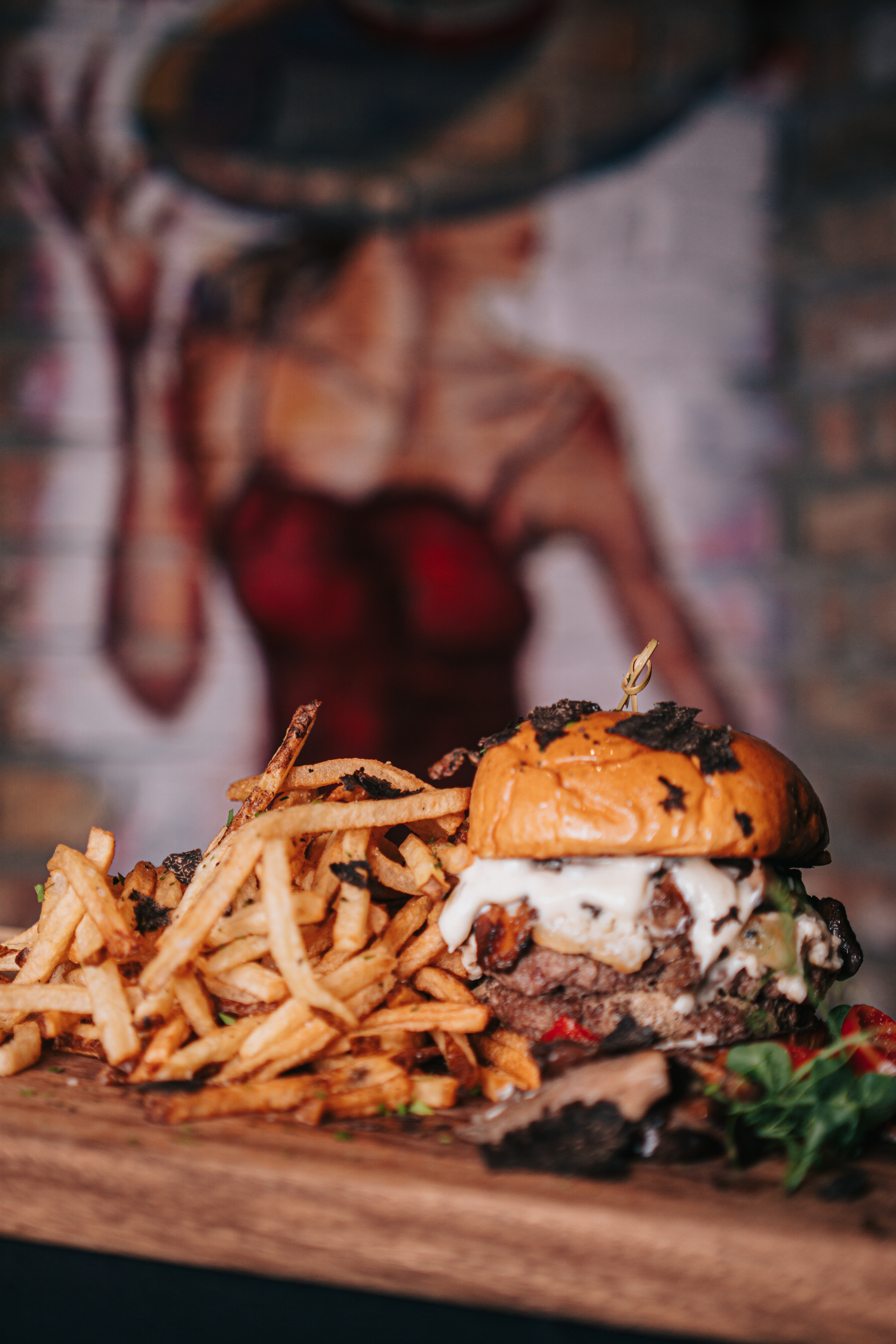 Rosland’s Legacy Burger with a side of fries, with a painting of Rosland in a red dress and hat in the background.