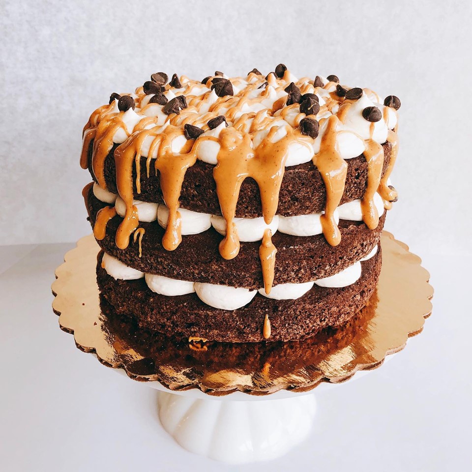 A three-layer chocolate cake with white fluffs in between the layers and topped with more white fluffs and dripping caramel sauce.