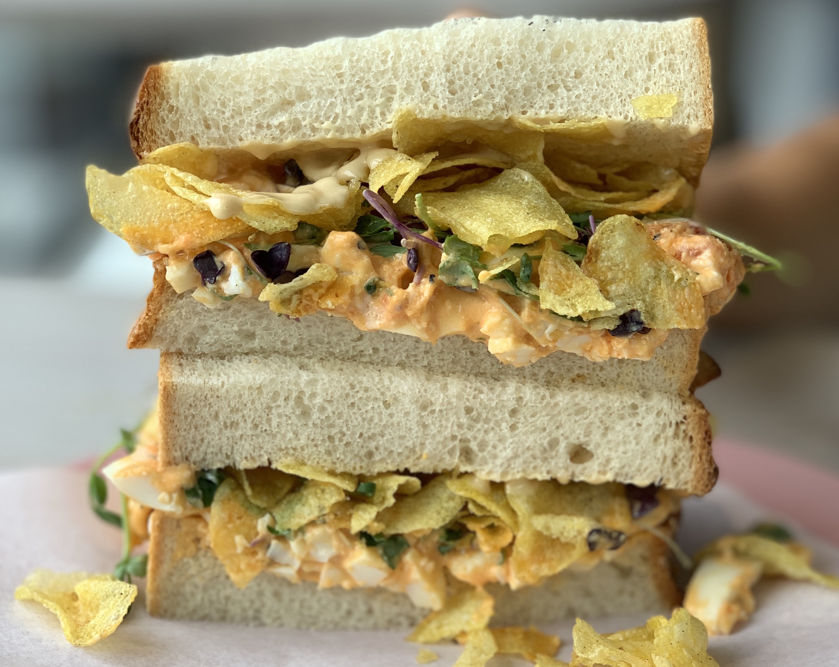 Two sandwiches stacked on top of each other, consisting of white bloomer bread filled with egg mayonnaise and crisps.