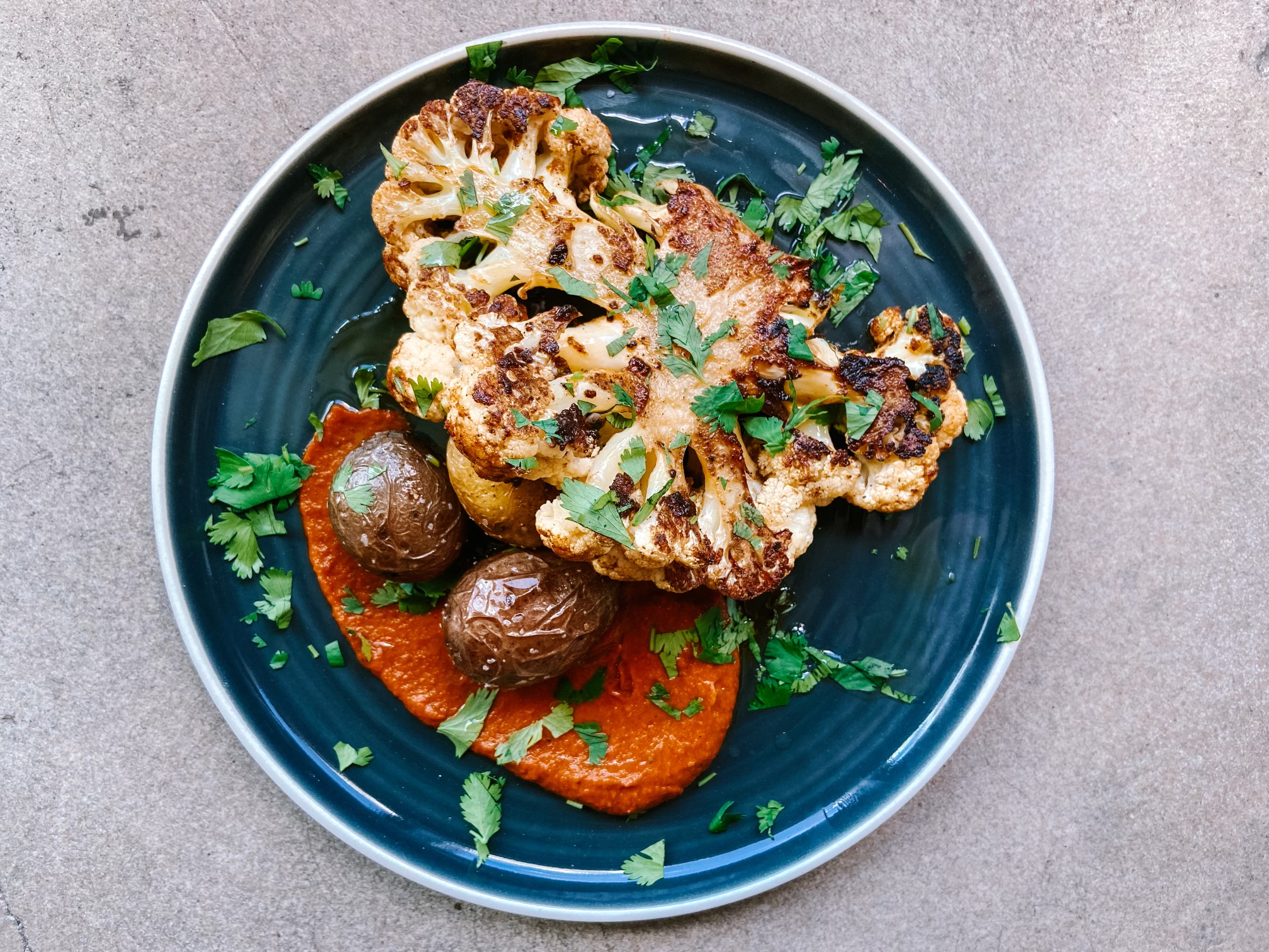 A big slice of cauliflower covered in herbs next to an orange sauce on a blue plate.