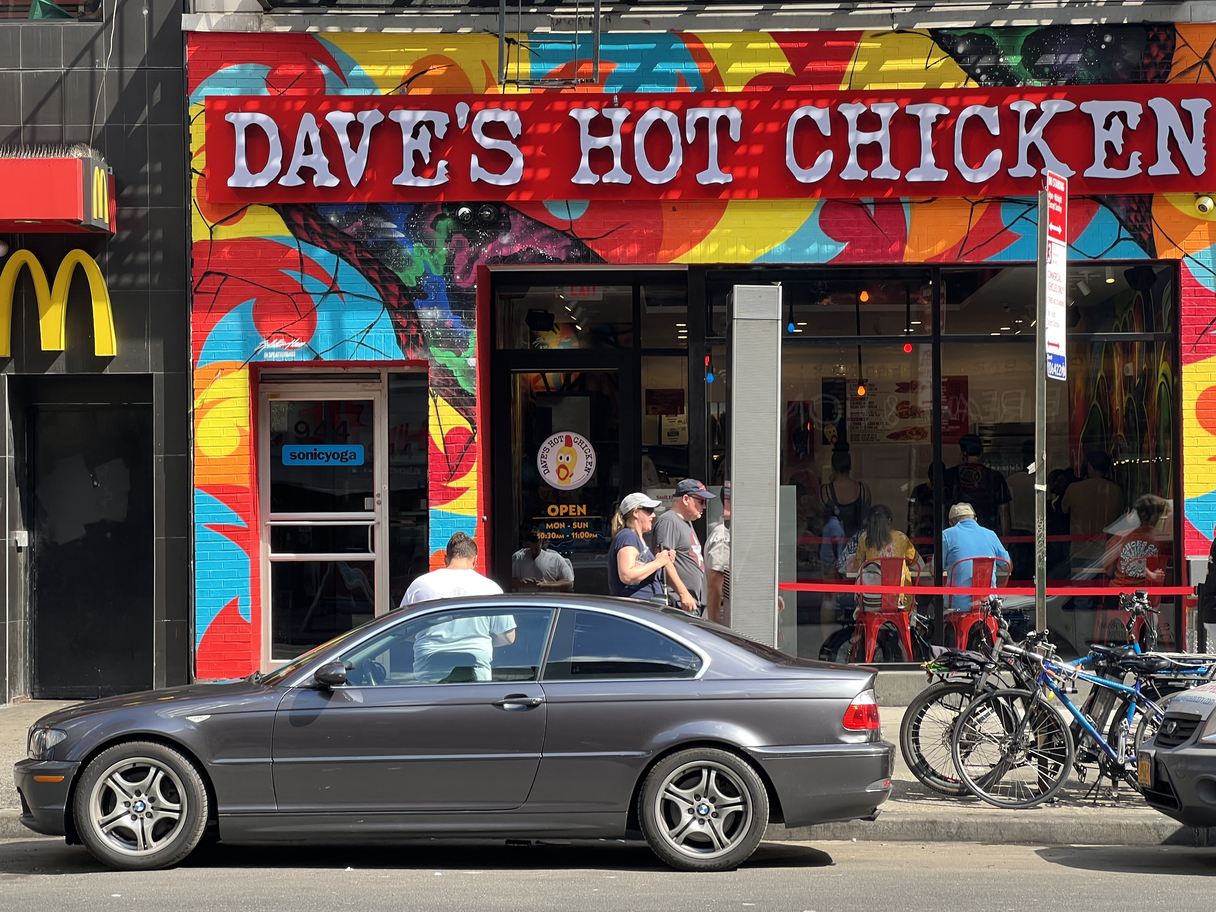 The multi-colored exterior facade of Dave’s Hot chicken is shown with pedestrians walking by