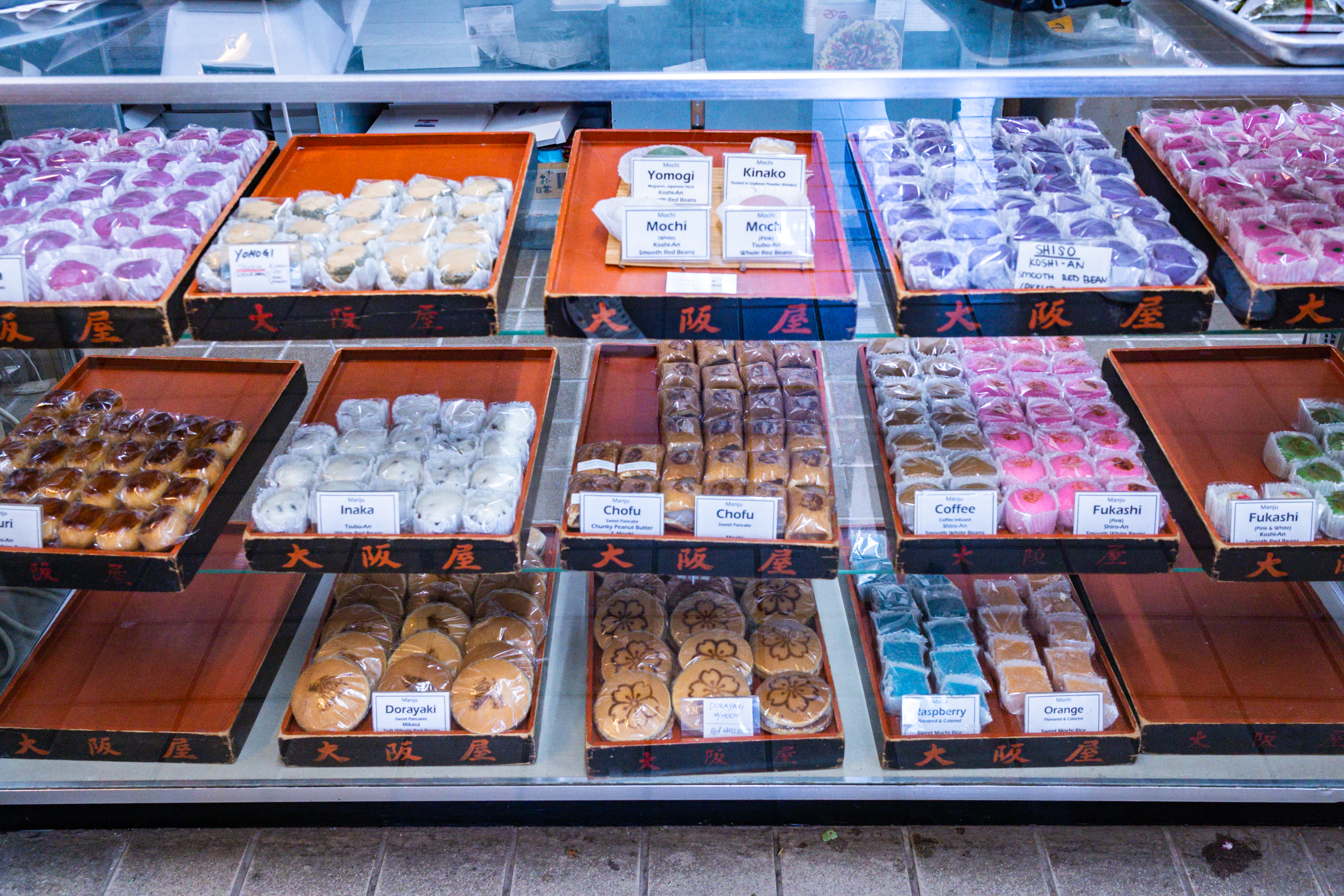 A pastry case filled with colorful wrapped mochi and other treats on trays.