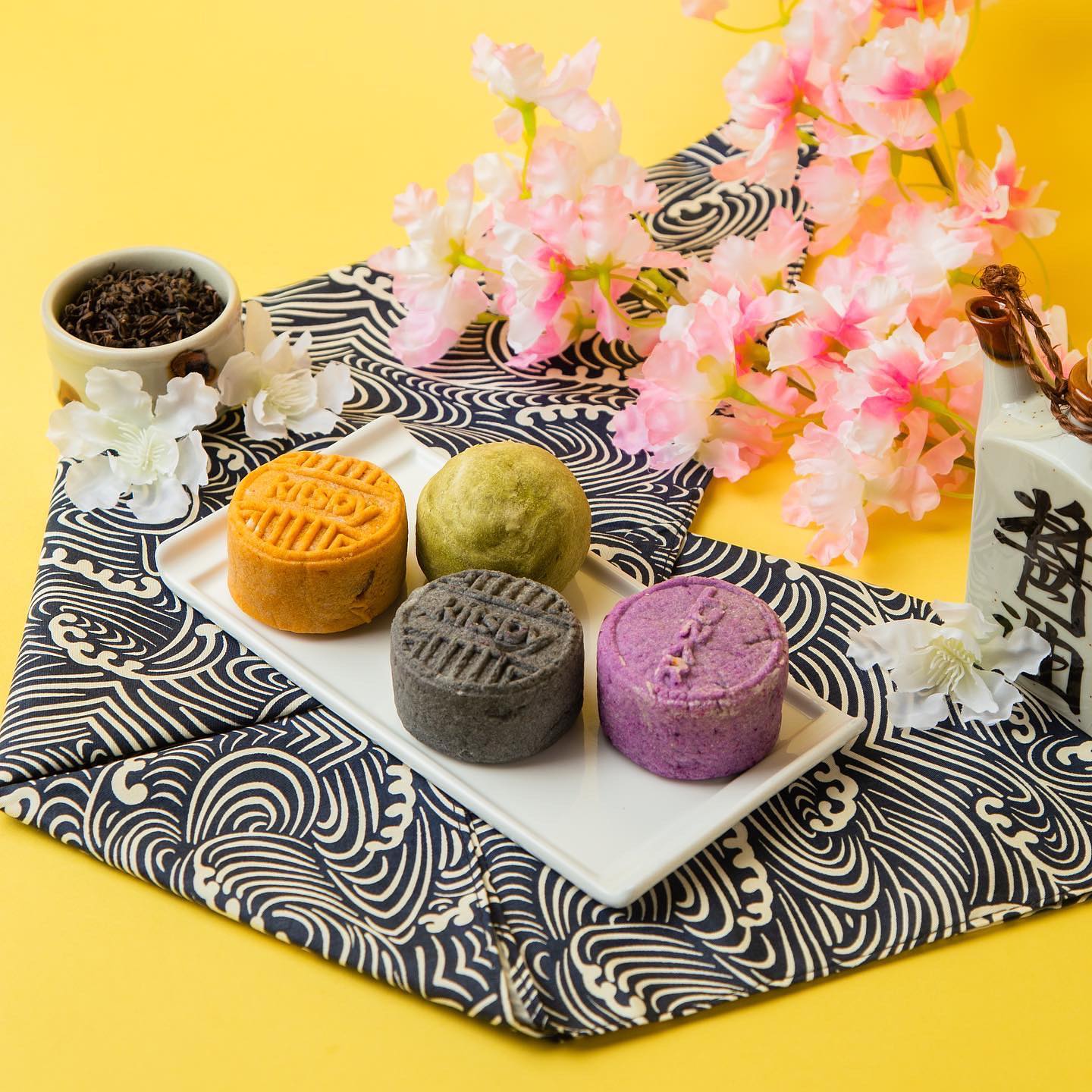Flowers and assorted mooncakes sit atop a napkin with black swirls.