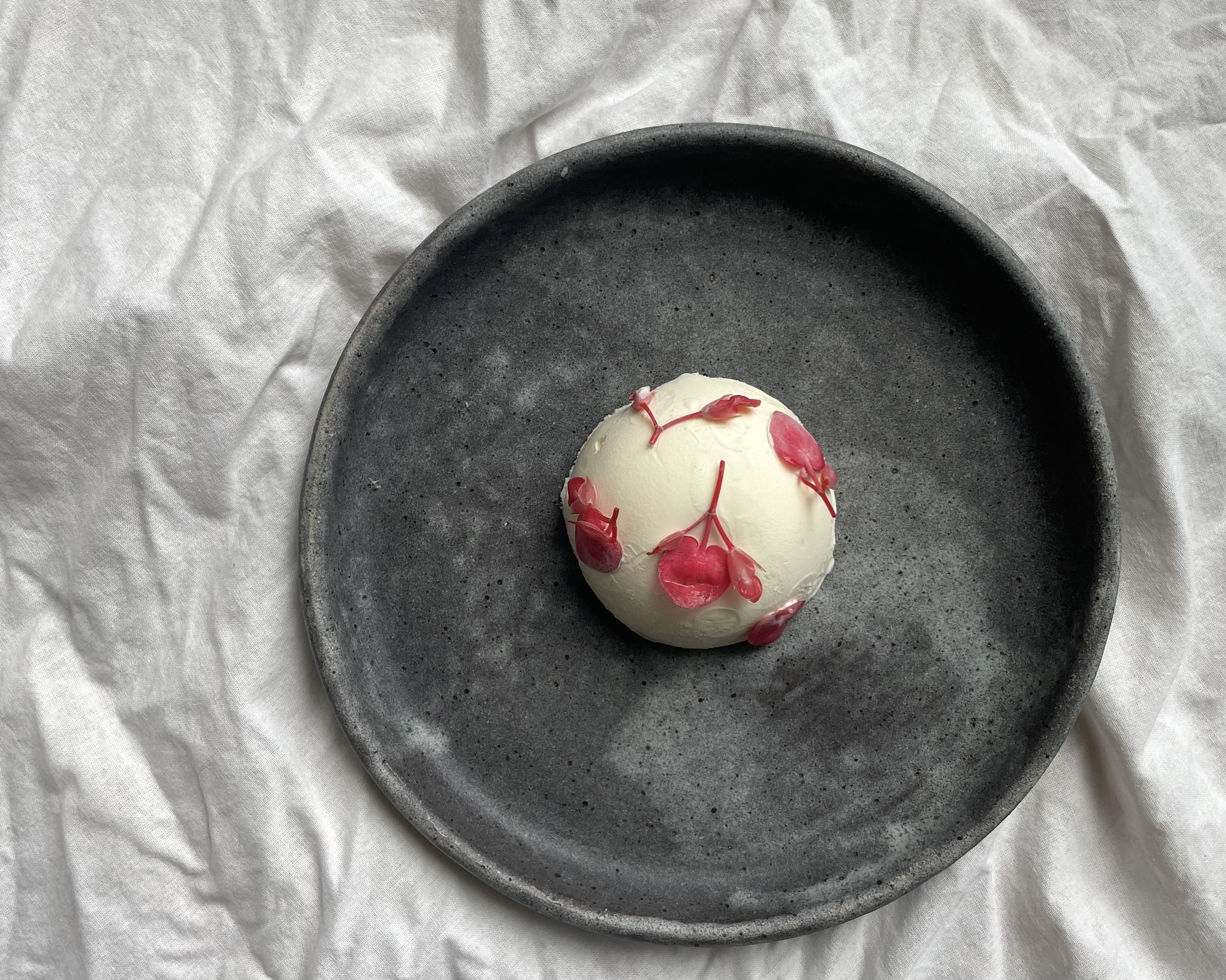 A gray ceramic plate features a white dome of ice cream with carefully-placed pink flowers.