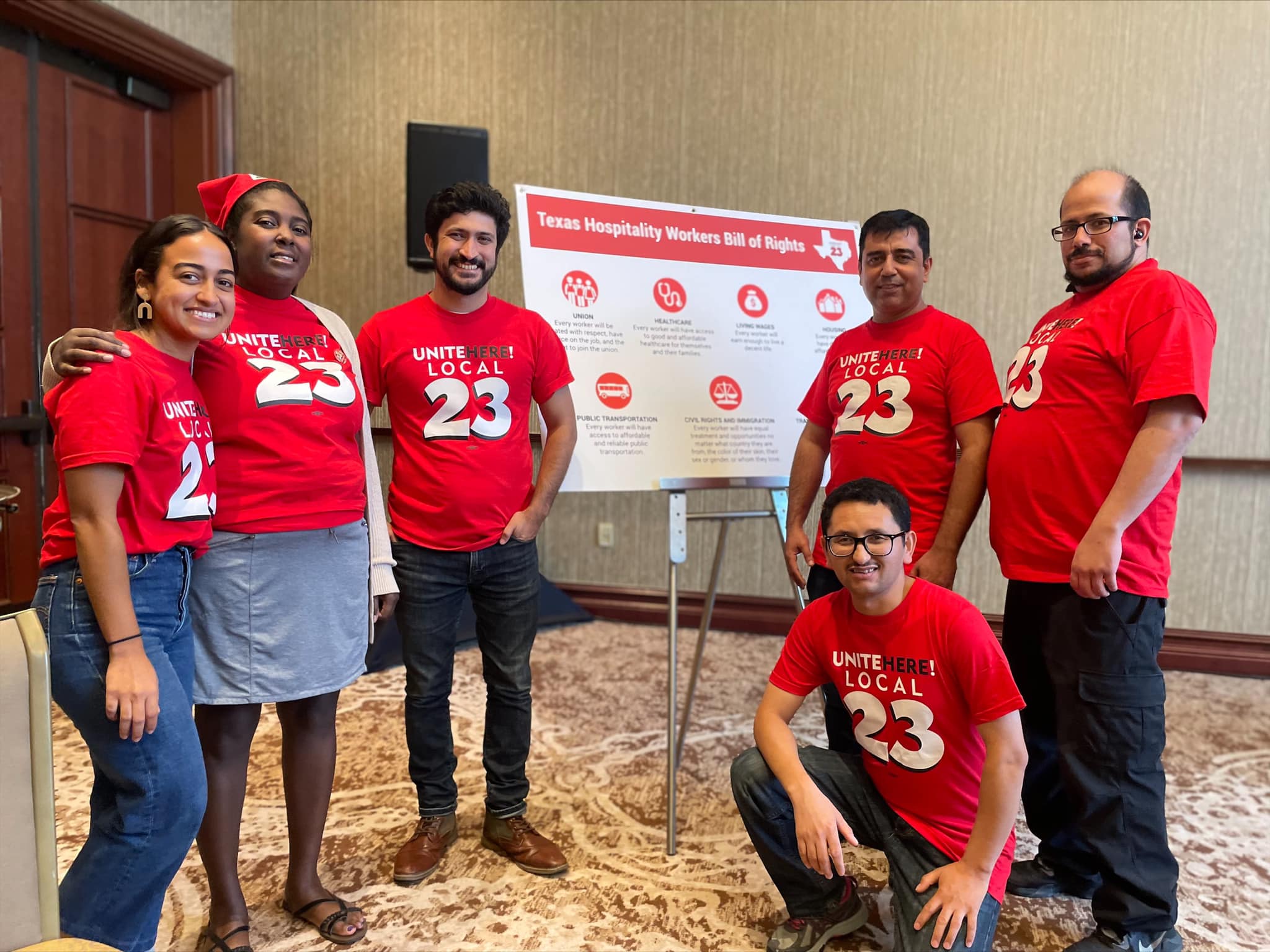 Six people wearing red union-related t-shirts standing in front of a poster board with text.