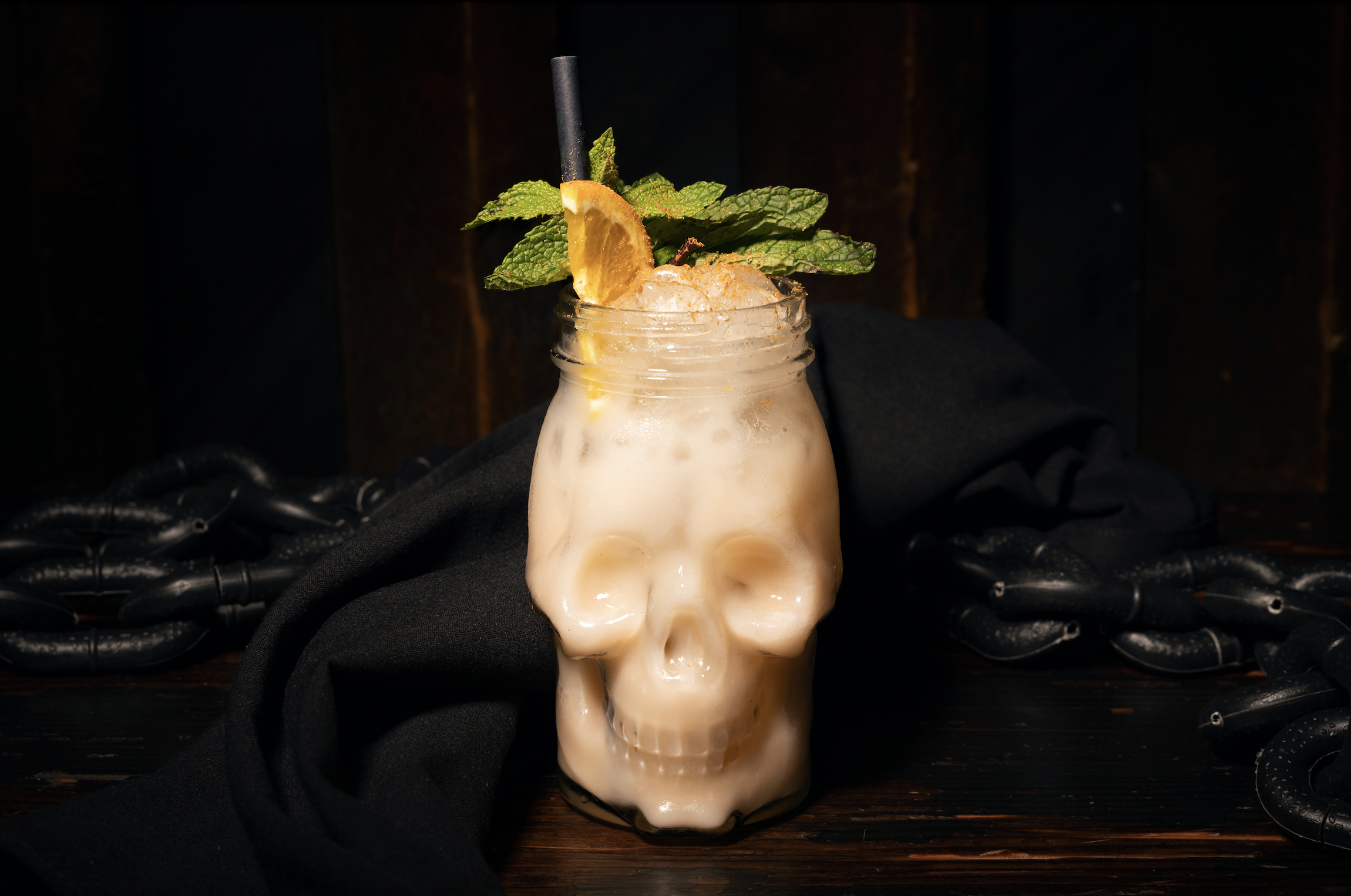 A cocktail with mint and an orange slice inside a skull-shaped glass.