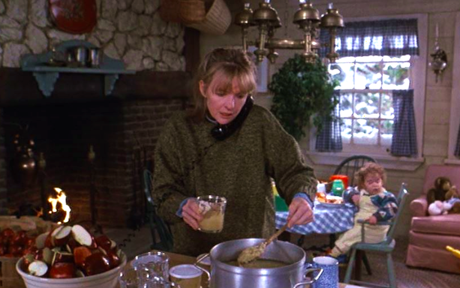 Still from “Baby Boom” showing Diane Keaton in a home kitchen spooning applesauce from a stovetop pot into a jar.