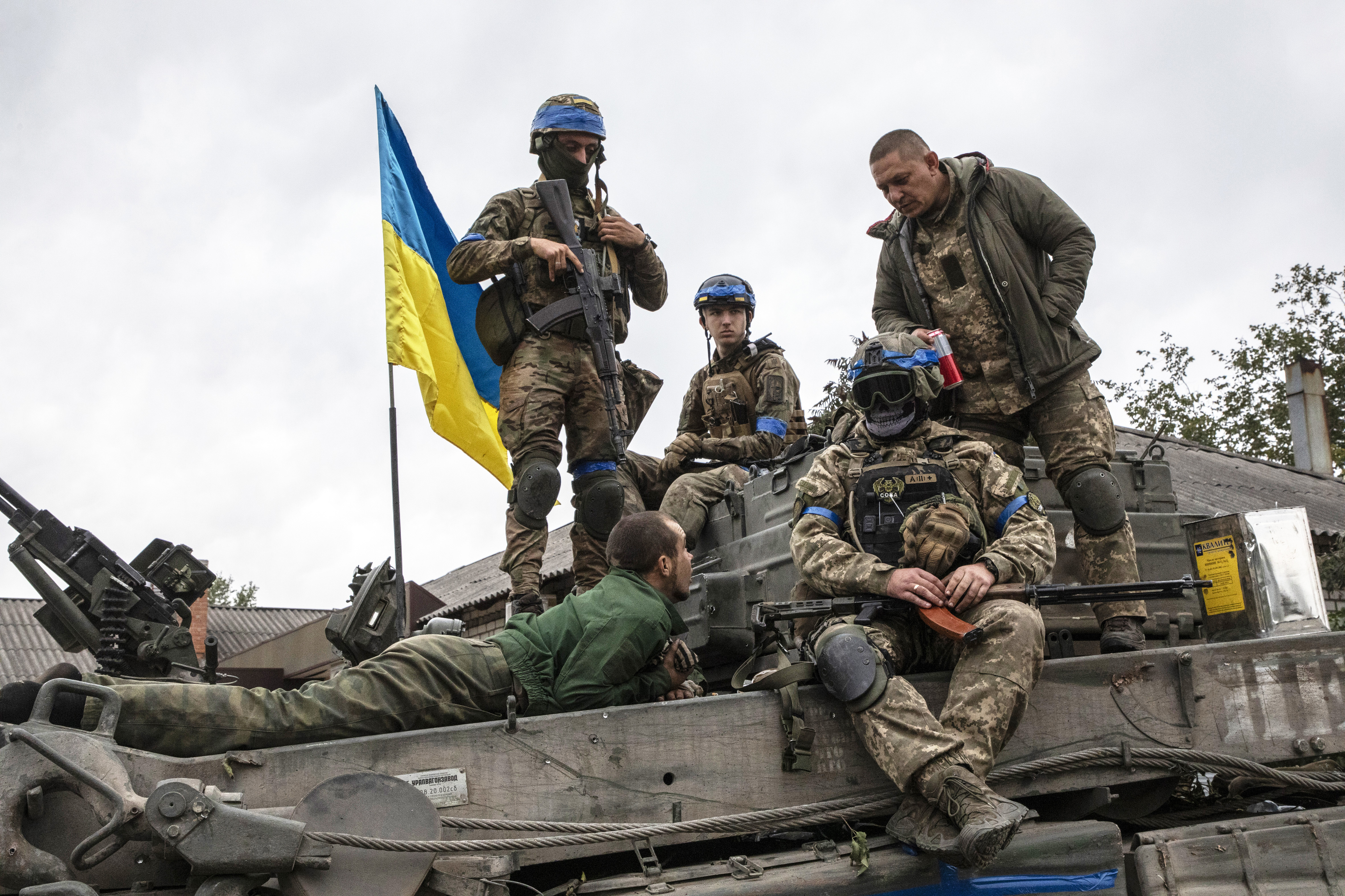 Several soldiers on top of a tank that flies a Ukrainian flag.