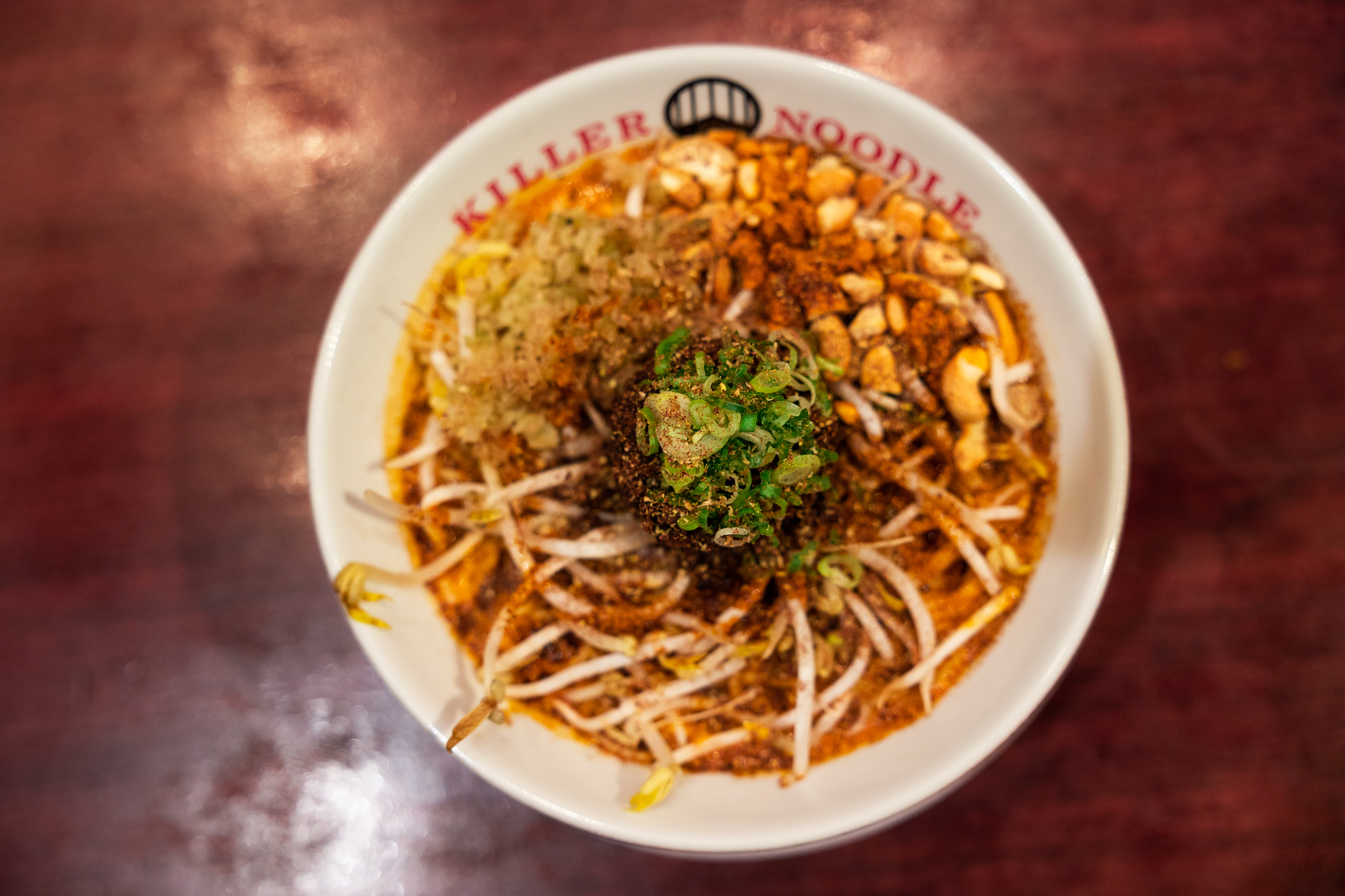 A bowl of Killer Noodle ramen topped with bamboo shoots, peanuts, corn, meat and cucumber.