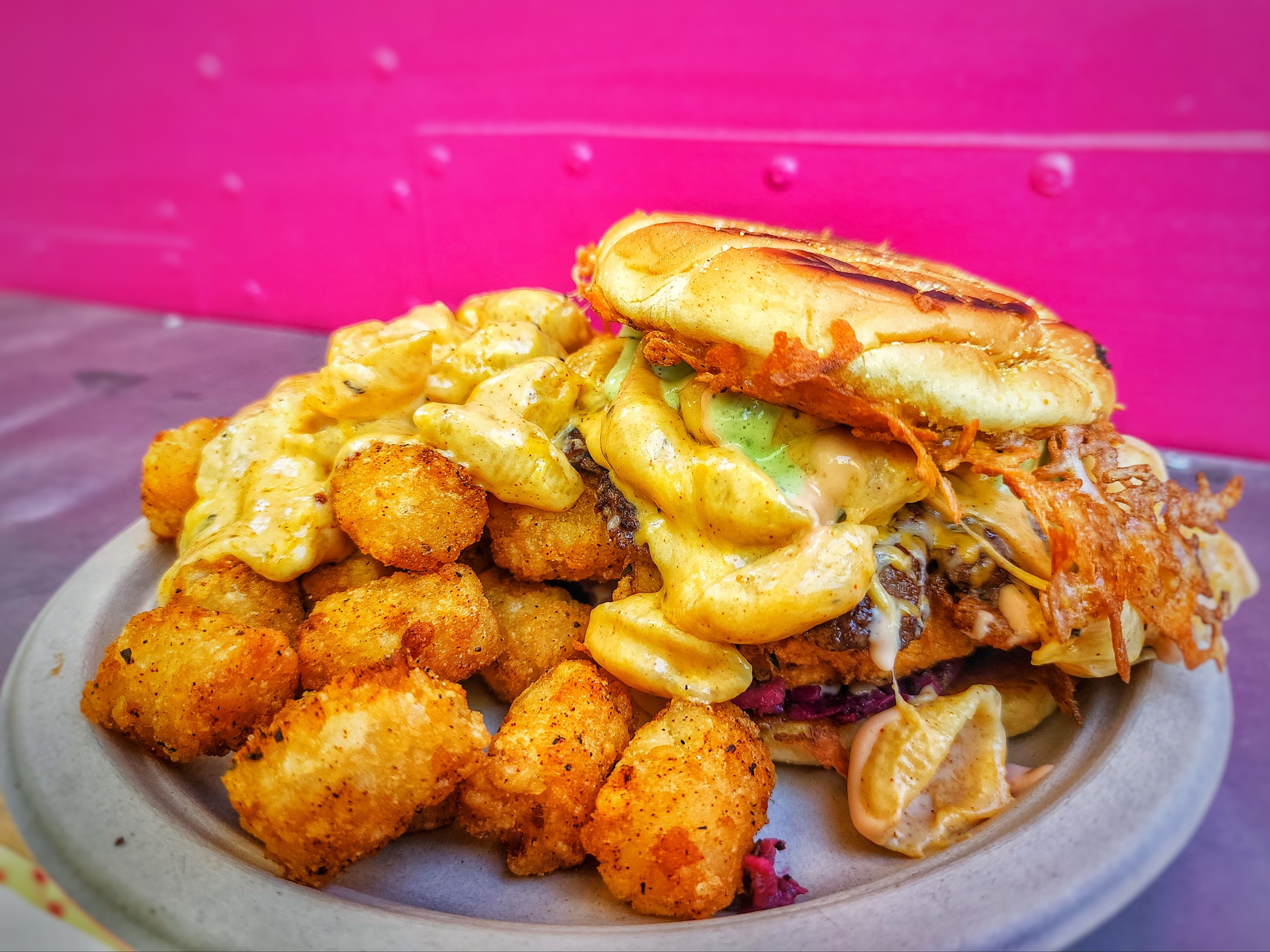 A burger topped with mac and cheese and fried chicken comes with a pile of tots at Nacheaux.