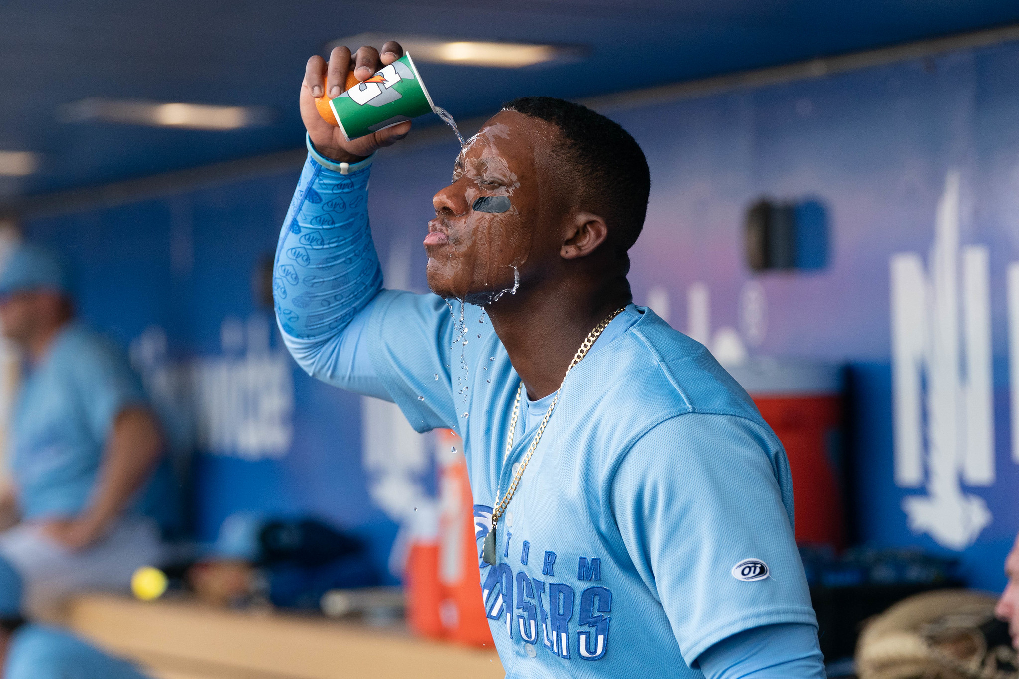A baseball player in a light blue jersey pours water from a green Gatorade cup all over his face.